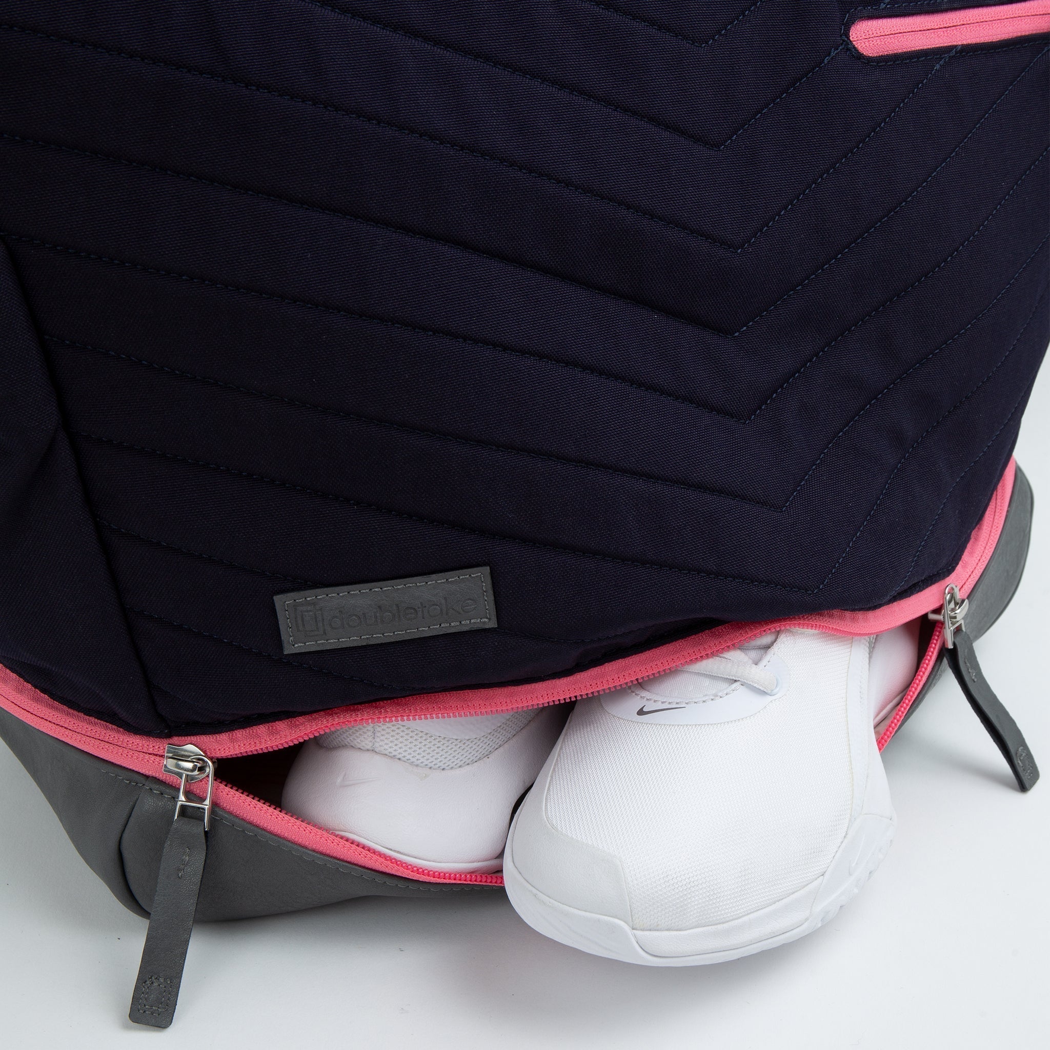 Dark blue pickleball tote by Doubletake, with a quilted pattern, pink zipper, and a lower grey compartment holding white sneakers.