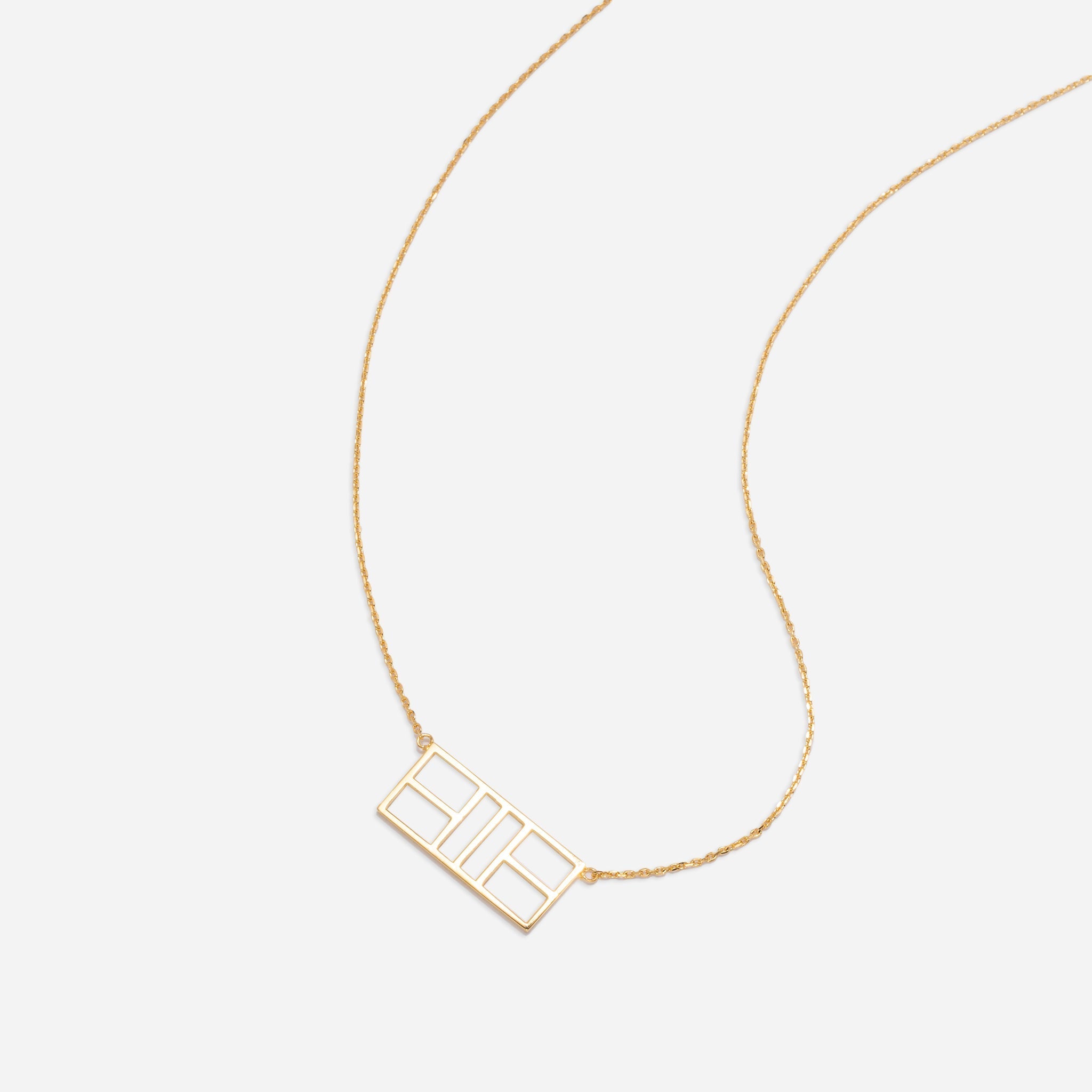 A gold necklace with a rectangular pendant with geometric cutouts.