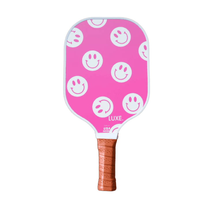 Pink pickleball paddle with white smiley face pattern. Brown handle.