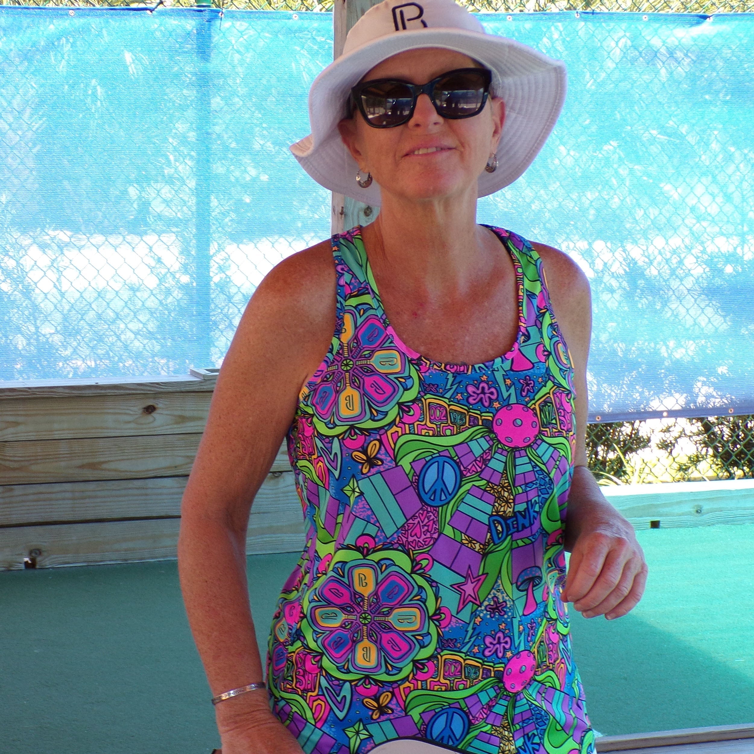Groovy Pickleball Racerback Tank by Pickleball Bella in vibrant colors with peace signs and paddles, worn by a woman.