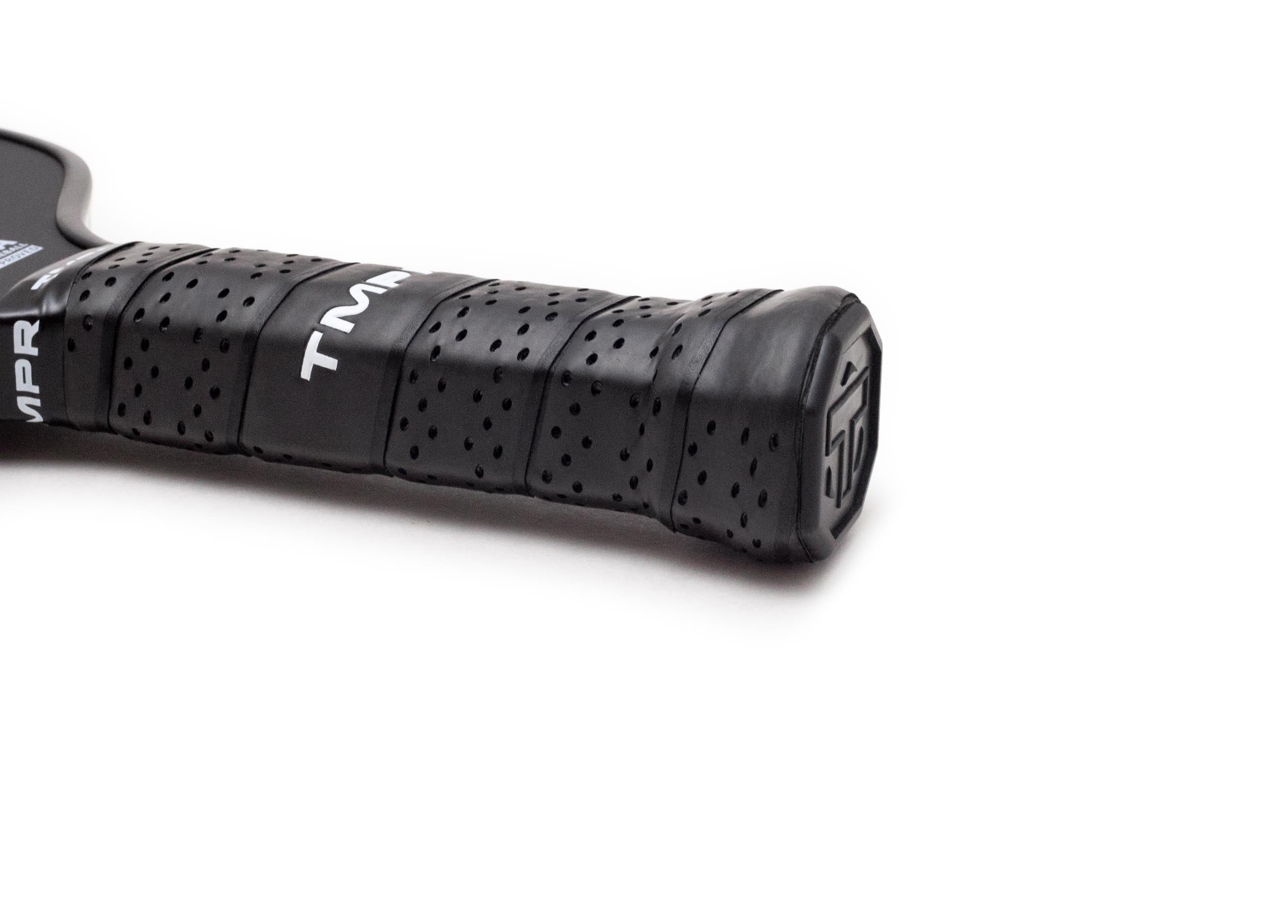 Black perforated grip of a pickleball paddle by TMPR Sports, with a 'TM' logo and textured butt cap.