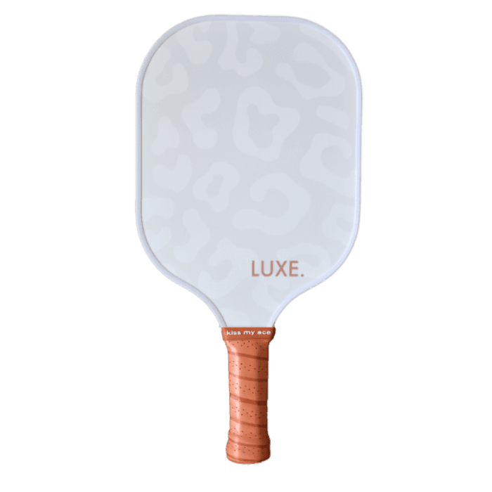 A pickleball paddle with a white face featuring light grey leopard spots, the word "LUXE" in a rose-gold color, a brown handle with ridges, and "kiss my ace" written at the handle base.
