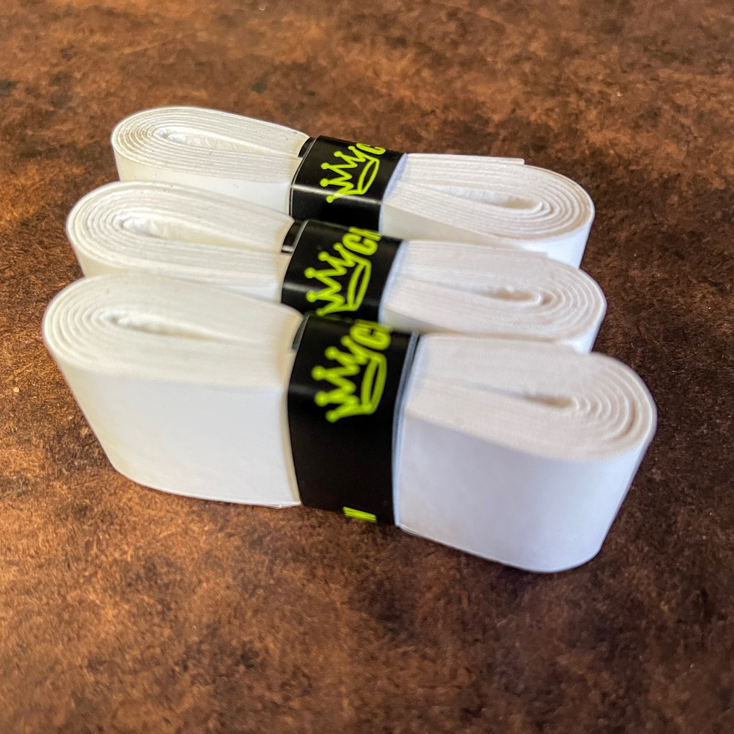 Three white tennis overgrips with black bands and green logos.