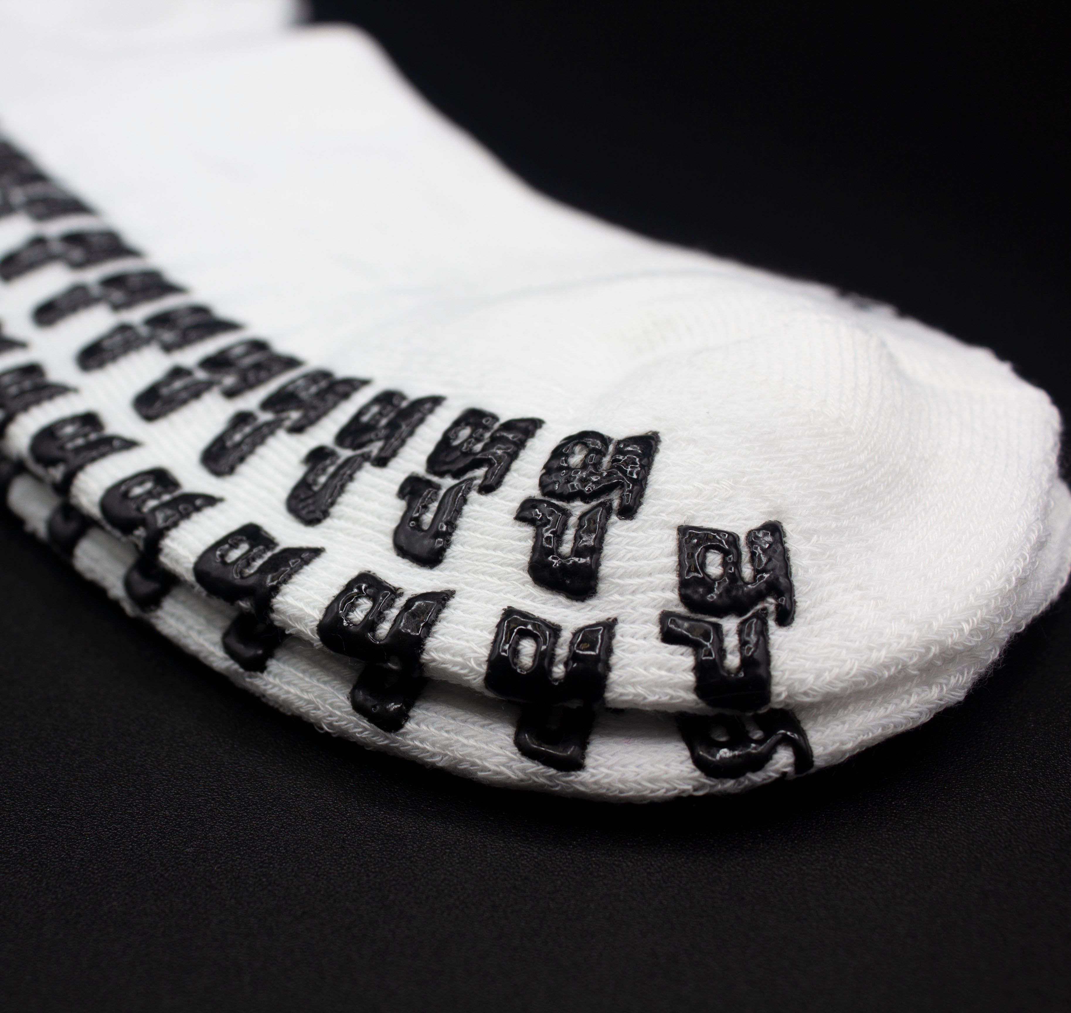 White Performance Socks with GRIPtech™ pattern by Bodhi Performance, featuring black textured non-slip grips on the sole, angled view.