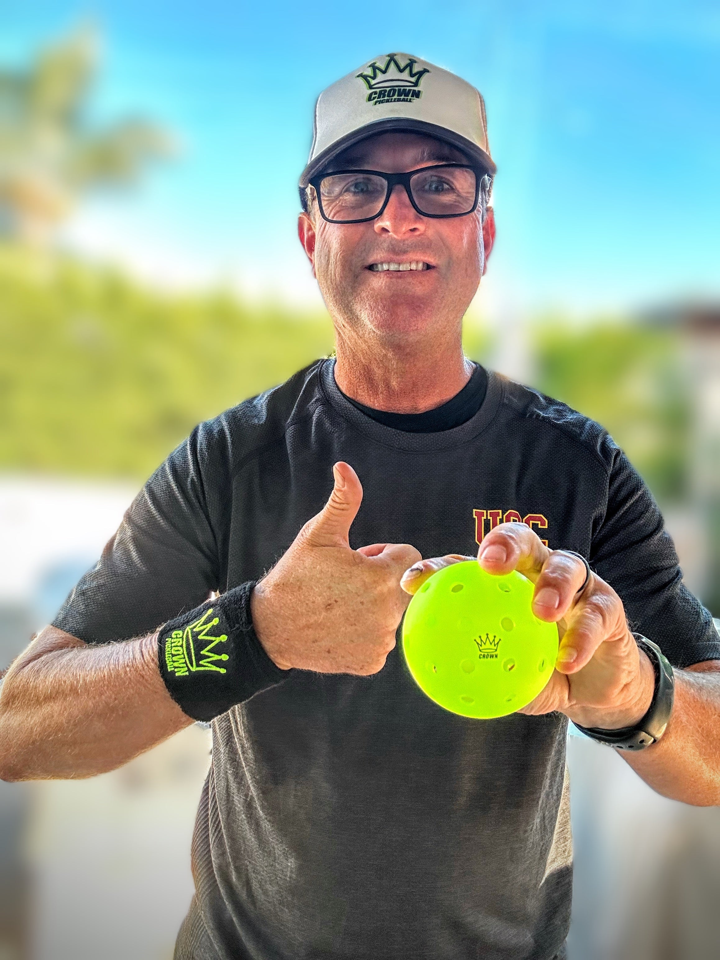 Man in a baseball cap and black shirt holding a yellow pickleball.