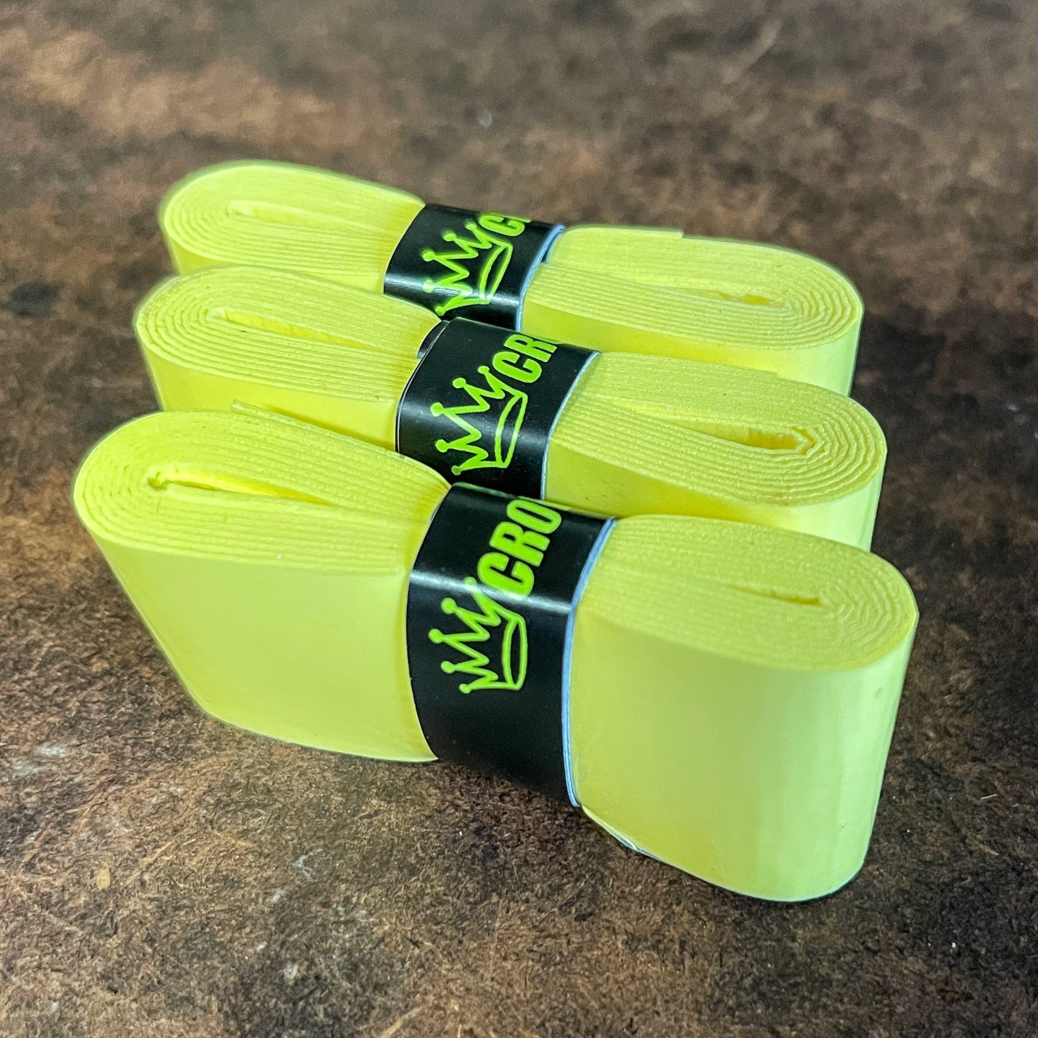 Three yellow tennis racket overgrips with black bands and neon green lettering.
