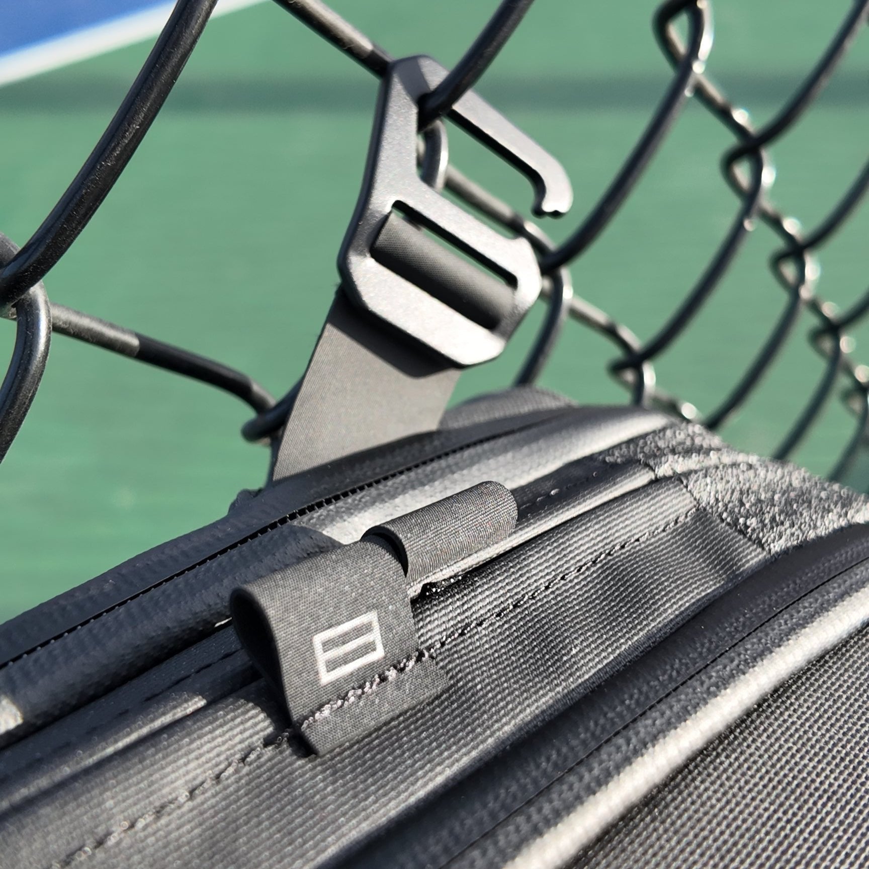 Dark grey pickleball sling by FORWRD hanging on a fence with a metal hook and logo tag.