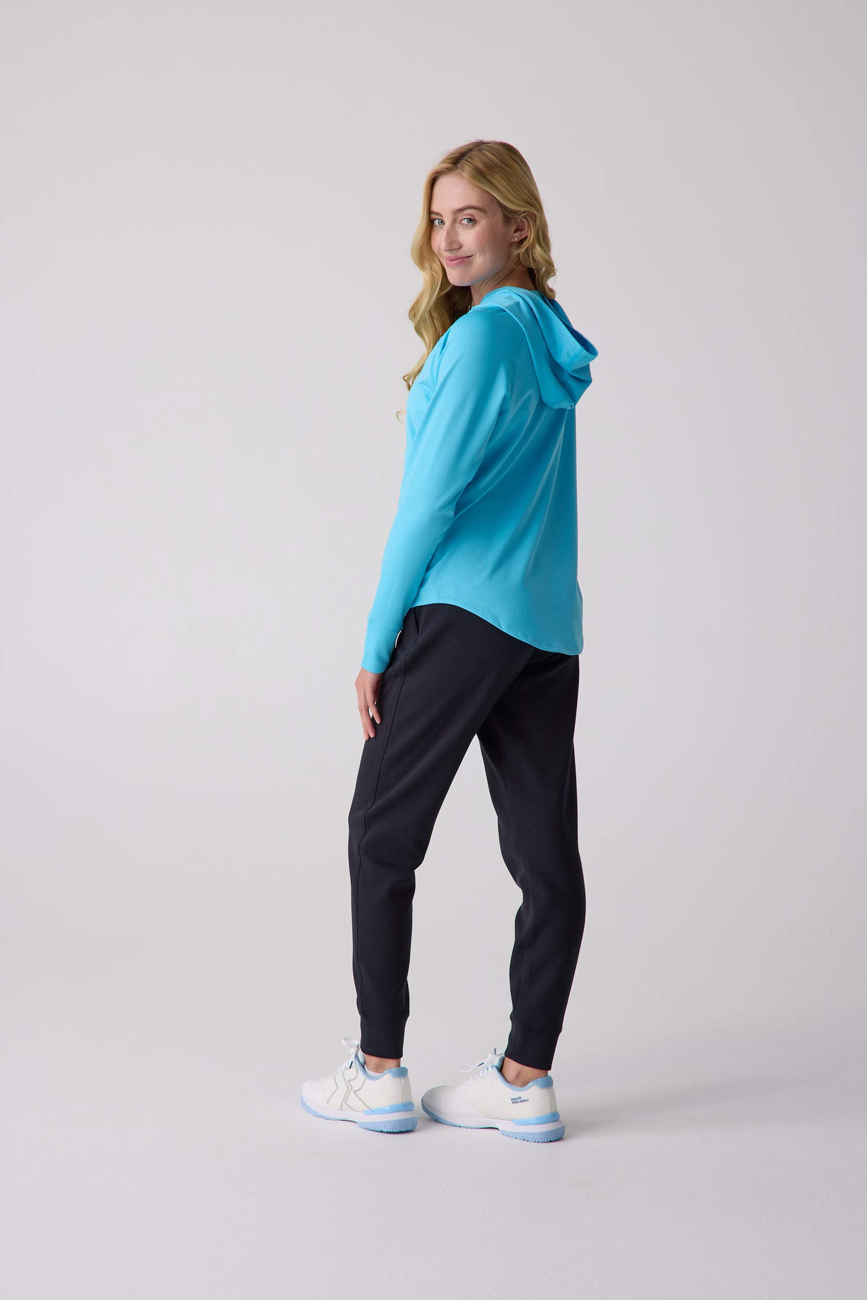 Women's layering hoodie in bright blue by Centerline Athletics, worn by a woman with dark joggers and white sneakers.