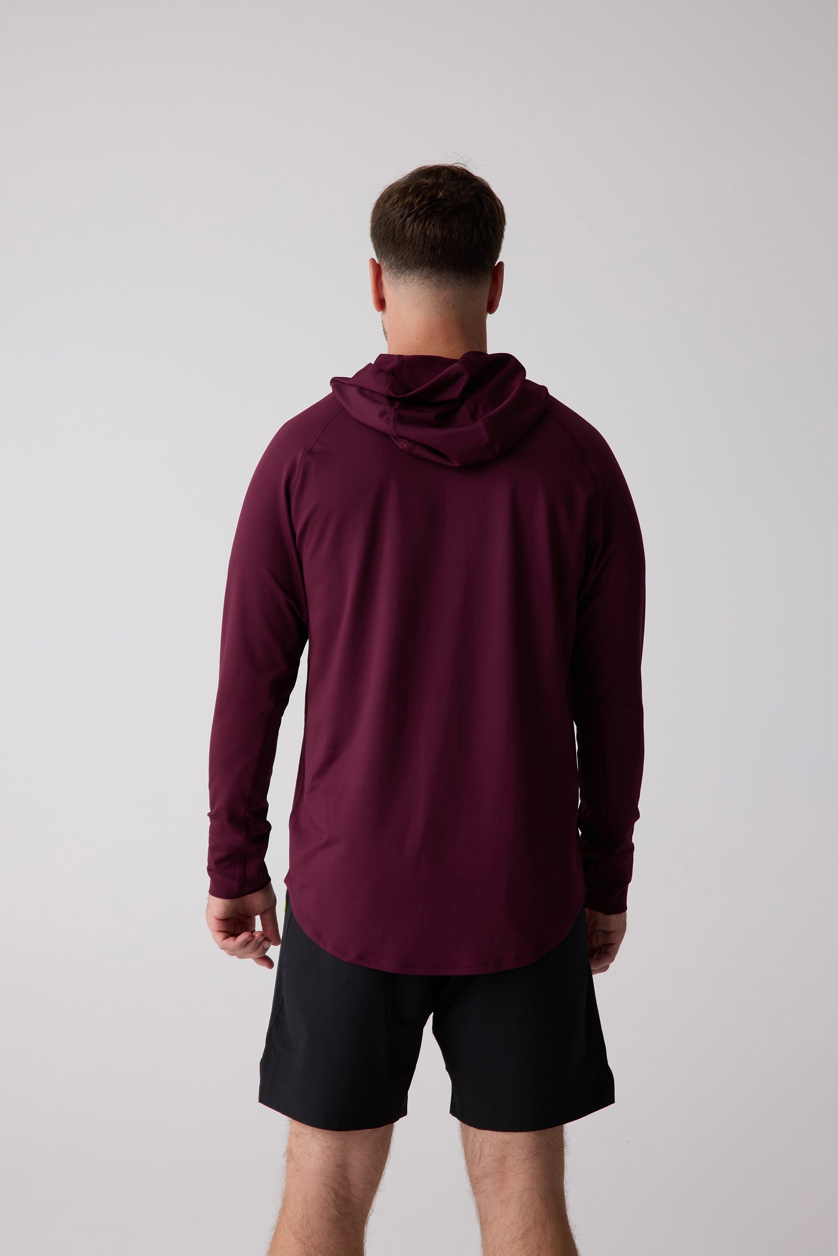 Maroon Men's Layering Hoodie by Centerline Athletics, viewed from the back, with long sleeves and a rounded hem, worn with black shorts.