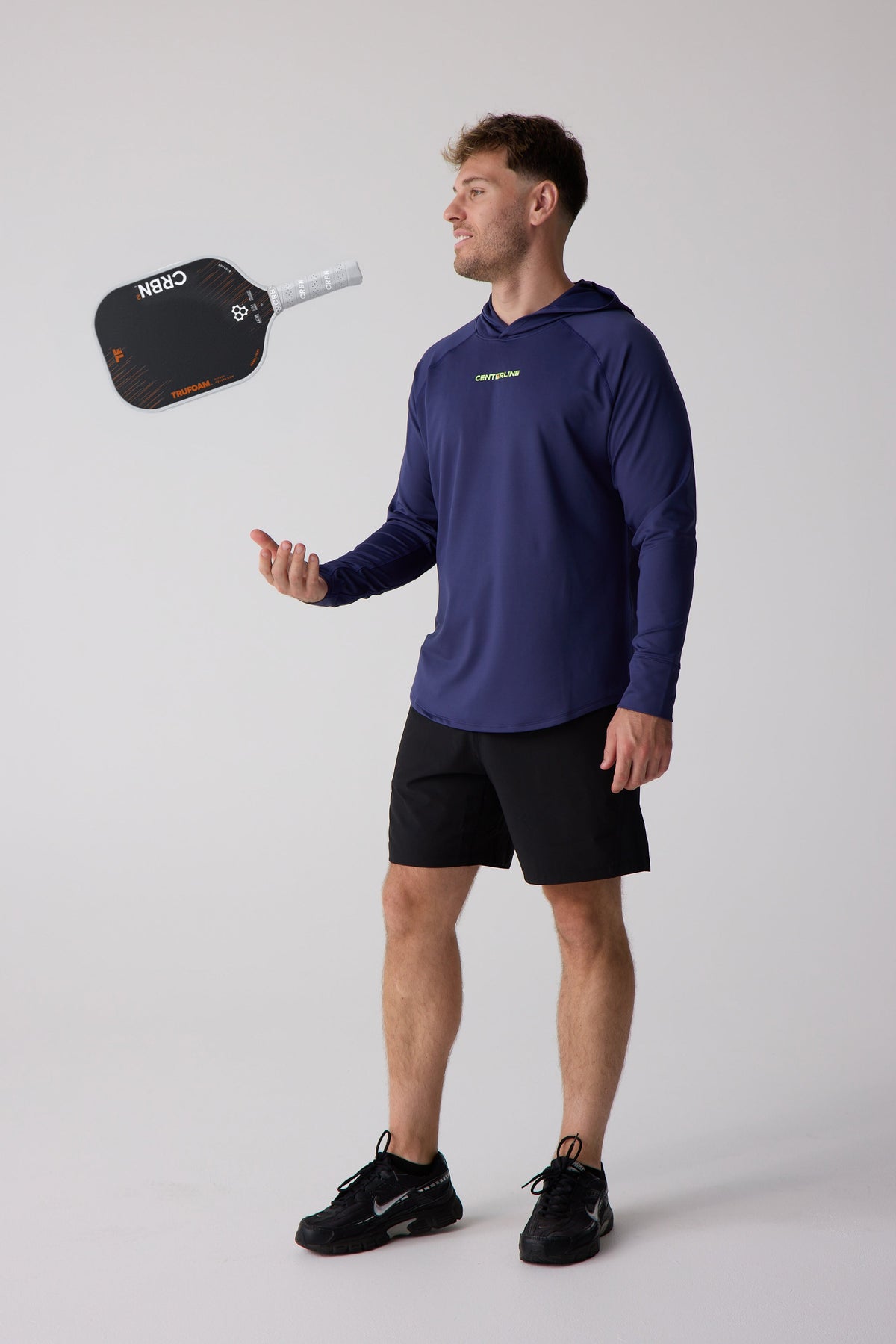 Navy blue men's layering hoodie by Centerline with neon yellow logo, shown in lifestyle side view with black shorts and athletic shoes.