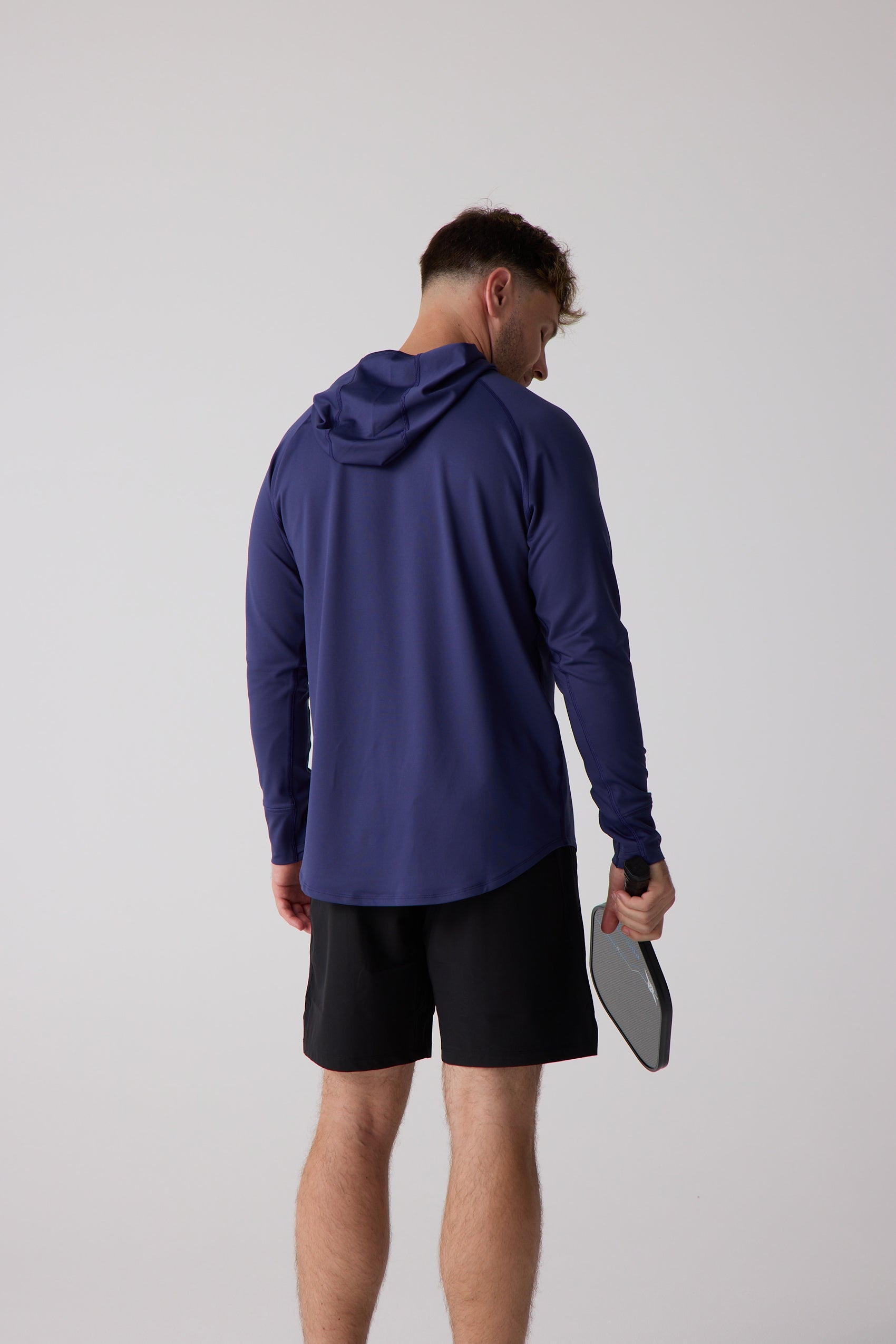 Navy Men's Layering Hoodie by Centerline Athletics, a long-sleeved hooded top on a man in black shorts holding a pickleball paddle, shown from the back.