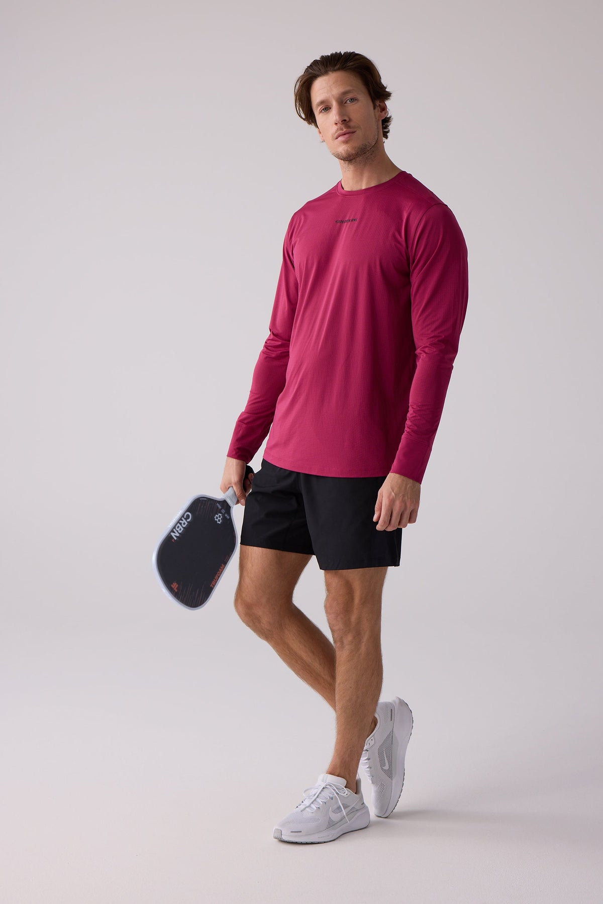 Burgundy textured long sleeve shirt by AirLite, featuring a crew neck and subtle chest logo, worn with black shorts and white sneakers in a full-body lifestyle pose.