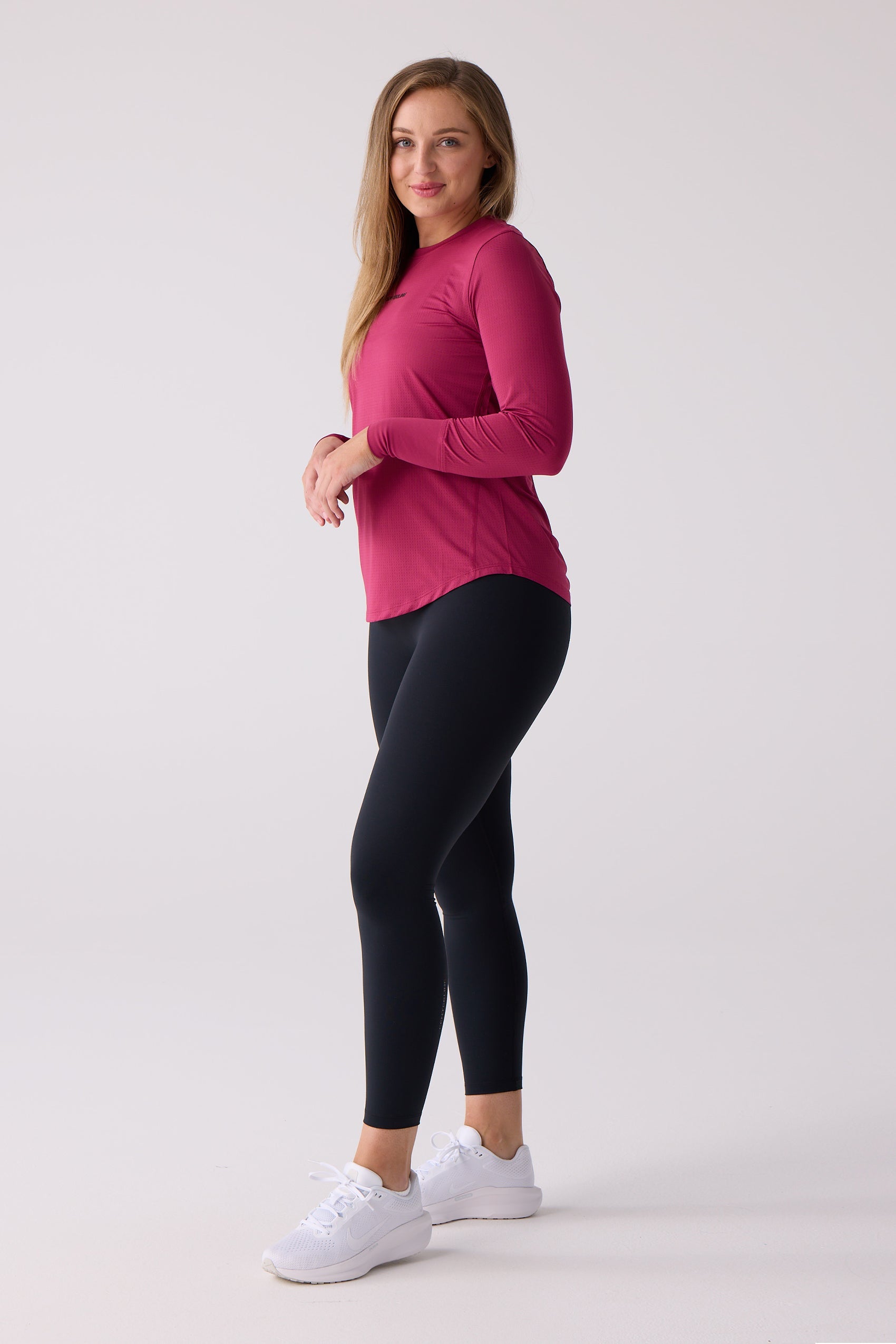 Magenta Women's AirLite long sleeve shirt by Centerline Athletics with subtle texture and rounded hem, styled with black leggings and white sneakers.