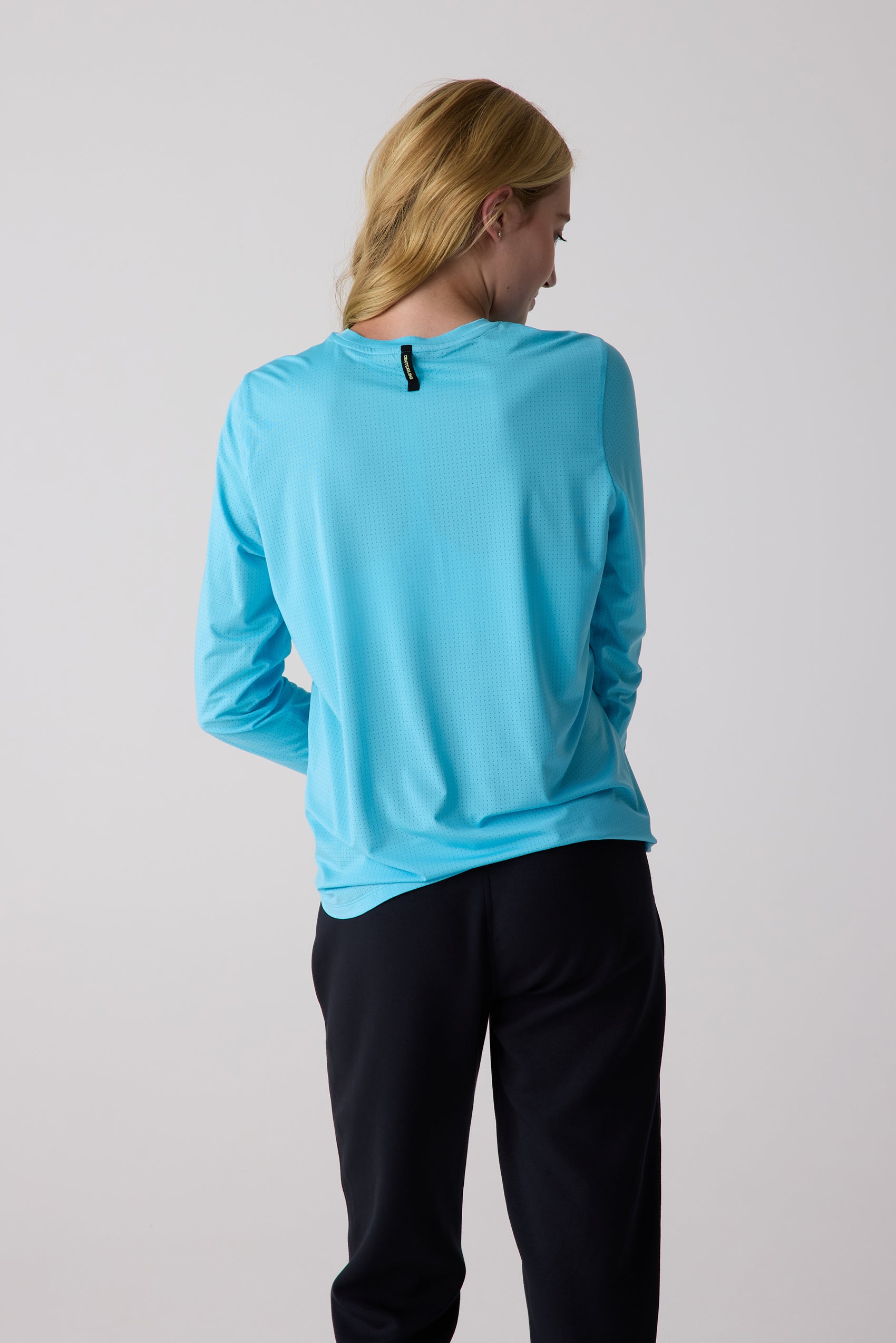 Light blue women's AirLite long sleeve shirt by Centerline Athletics with a perforated texture, shown from the back, paired with black pants.