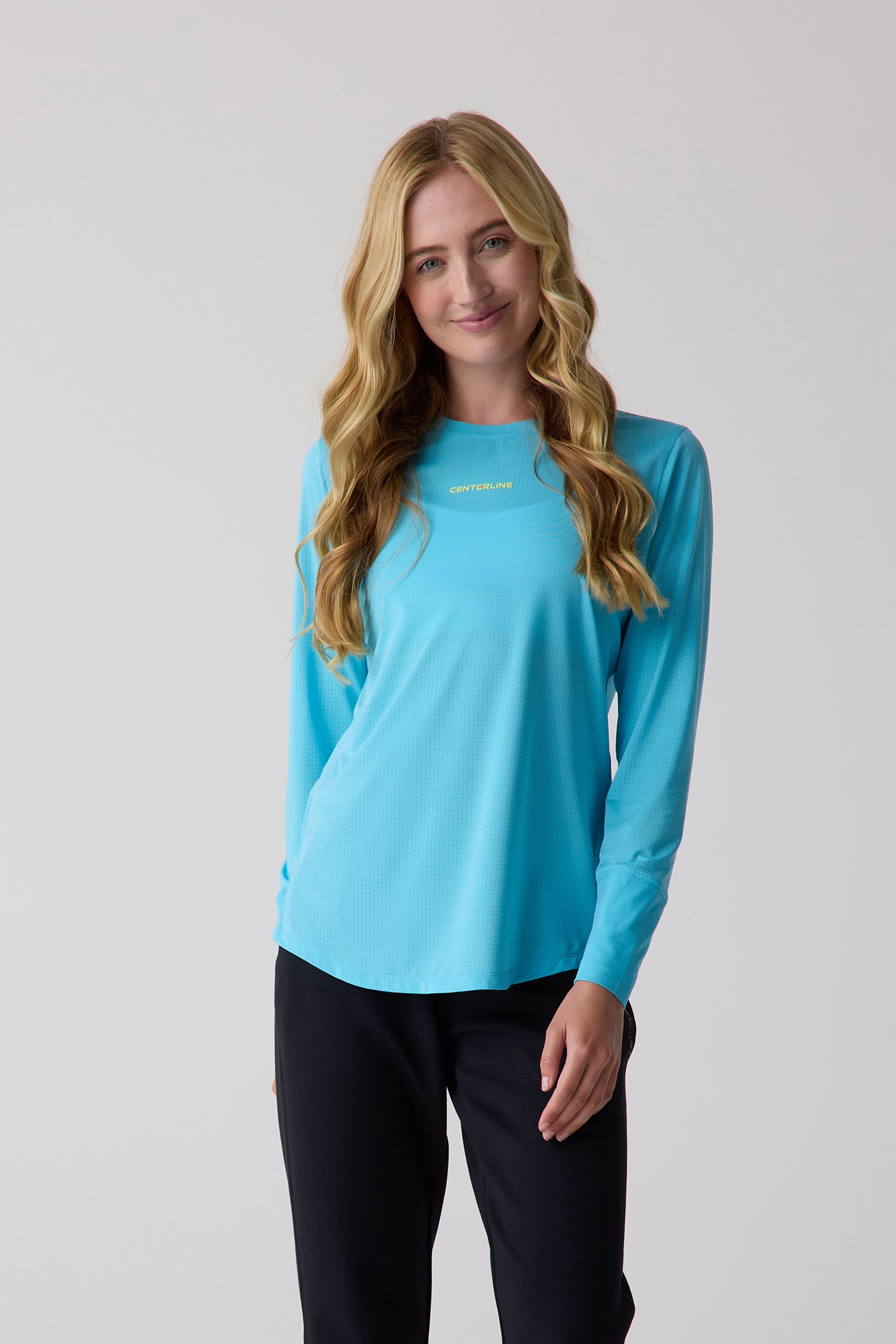 Women's blue AirLite long sleeve shirt by Centerline Athletics with a perforated texture and subtle logo on the chest, worn by a smiling model in black pants.