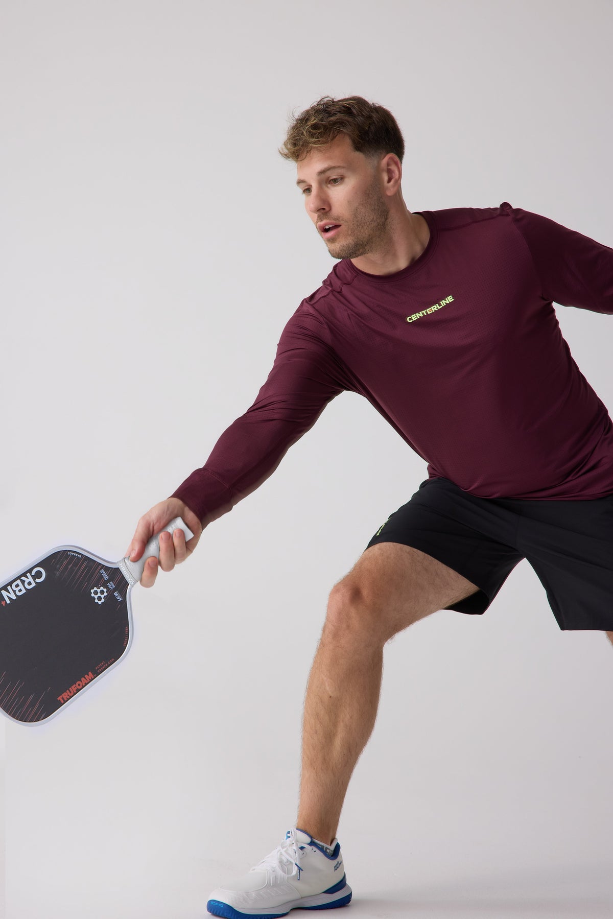 Burgundy men's long sleeve performance shirt by Centerline, featuring mesh texture and neon logo, worn during active pickleball play.