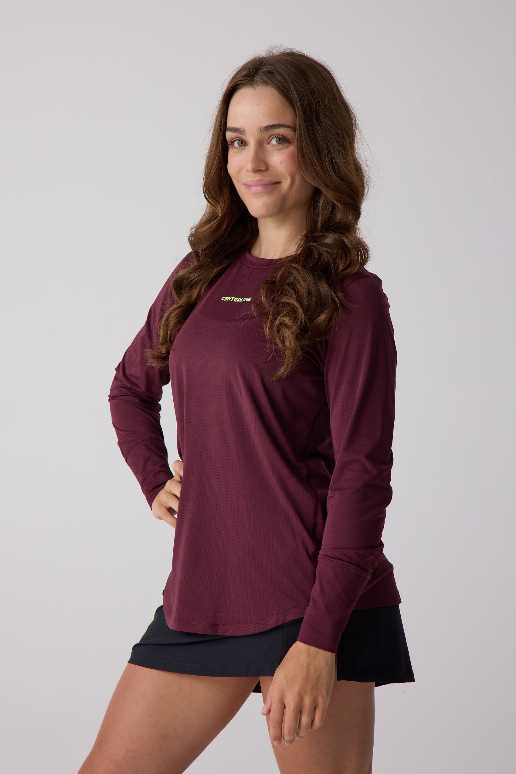 Maroon Women's AirLite Long Sleeve by Centerline Athletics, with a perforated texture and lime green logo, worn with a black skirt.