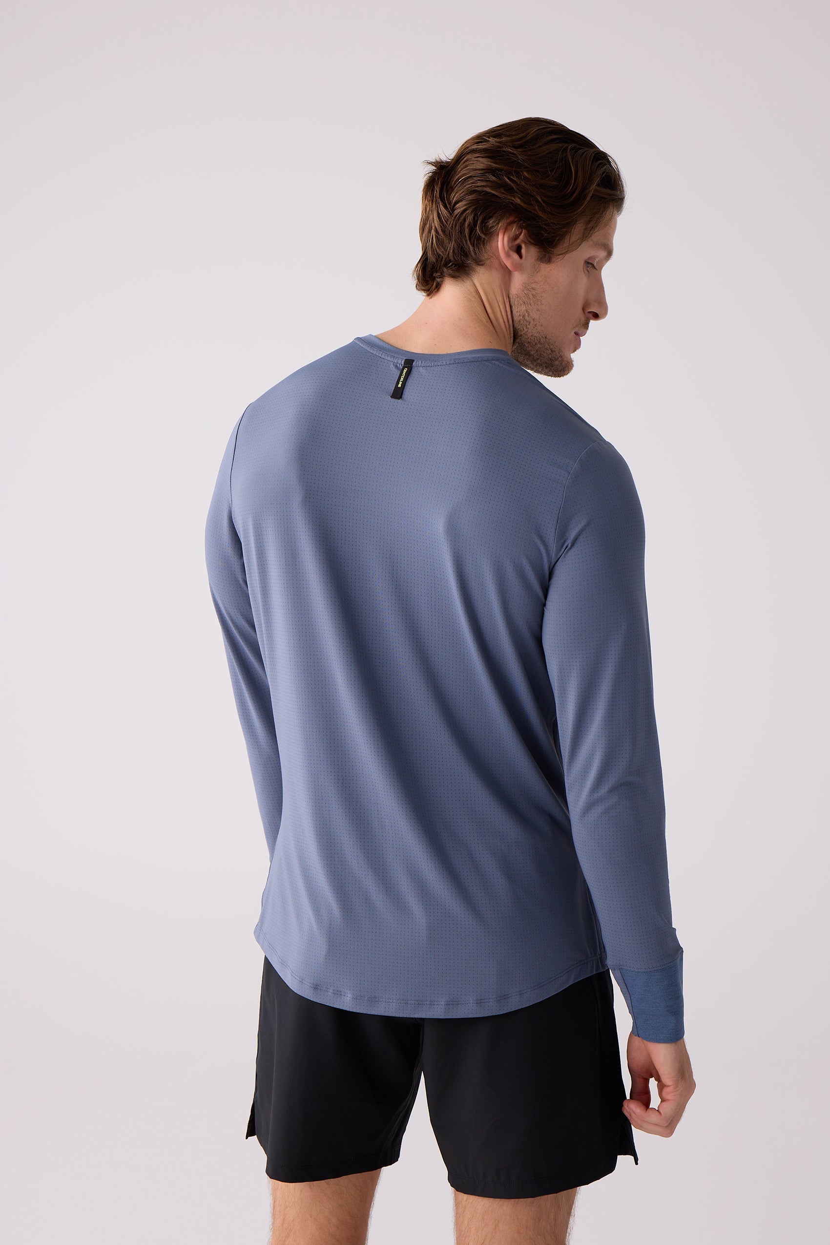 Men's blue long sleeve shirt by Centerline Athletics, back view, with perforated texture and yellow-tagged neck, worn with black shorts.