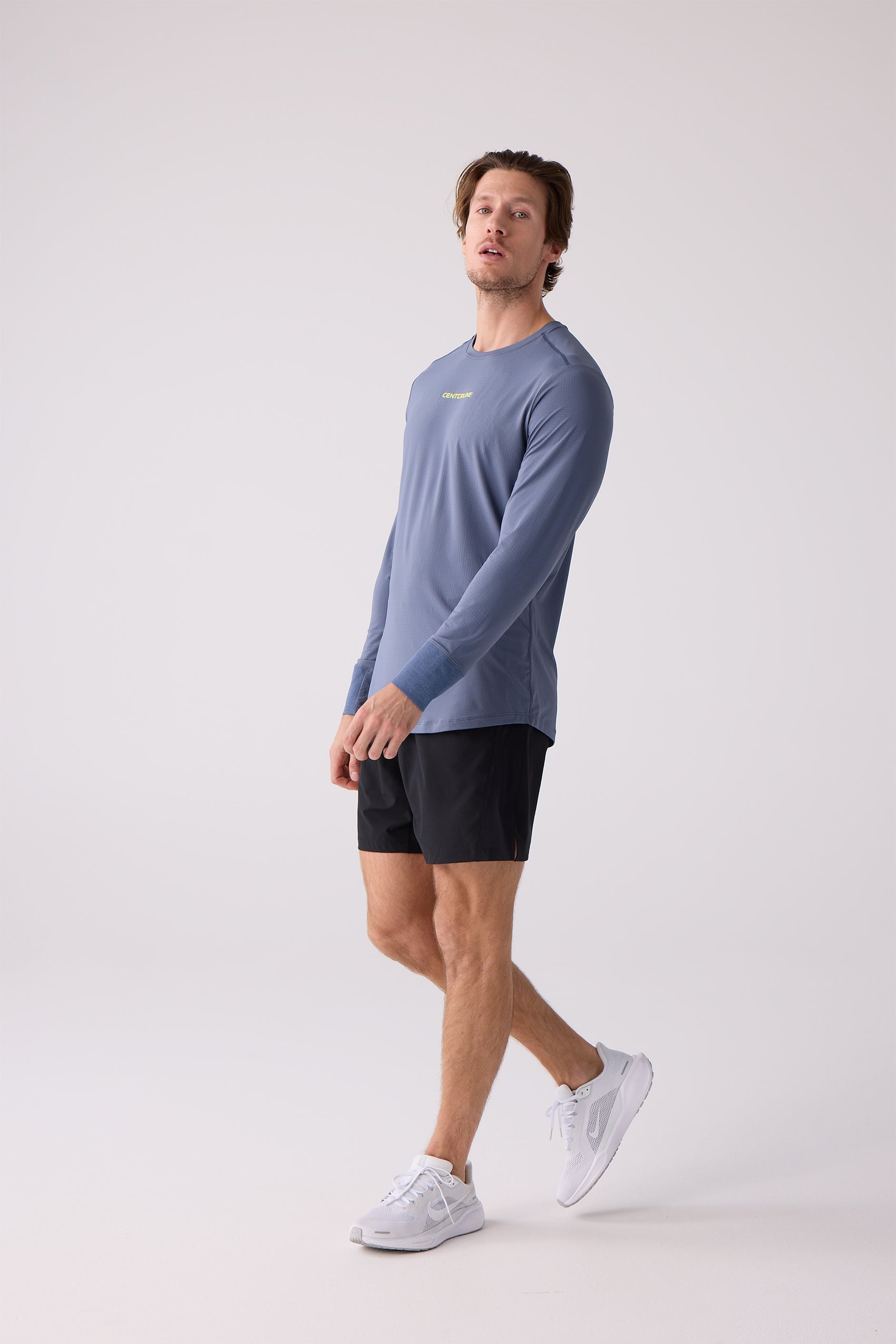 Men's slate blue long sleeve shirt by Centerline Athletics with textured fabric, yellow CENTERLINE logo, and thumbholes, worn with black shorts and white sneakers.