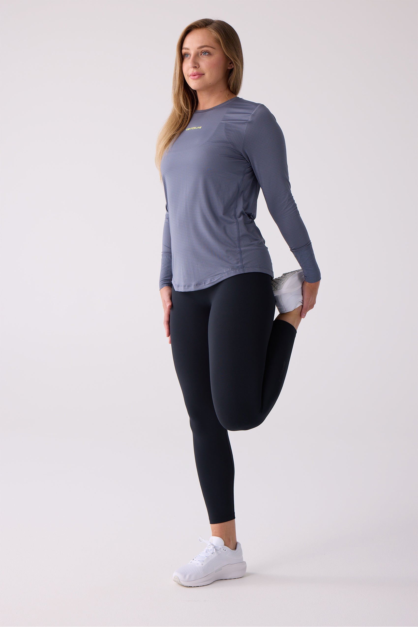 Women's dusty blue-grey AirLite long sleeve shirt by Centerline Athletics, with perforated texture and yellow logo, worn while stretching.