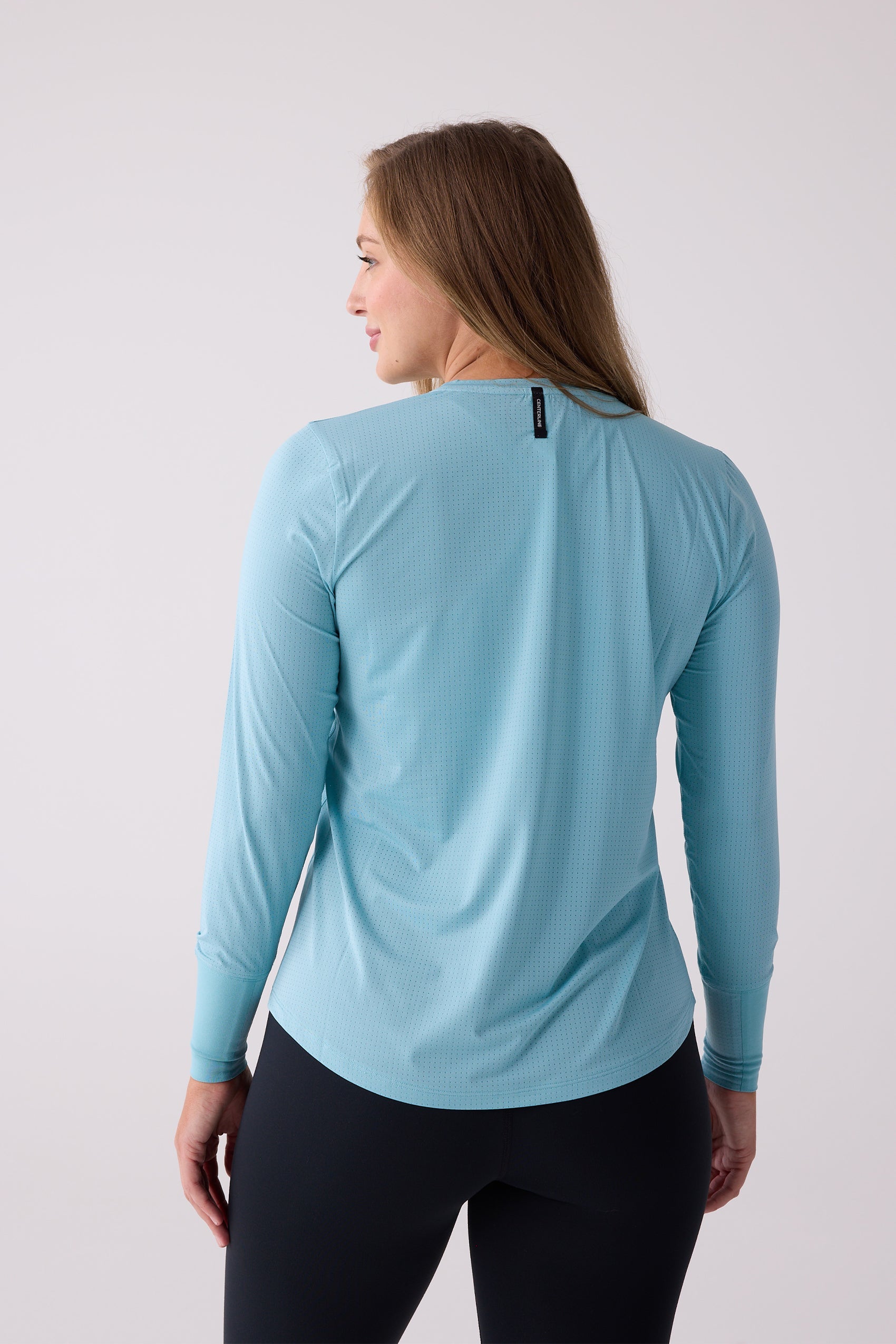 Light blue perforated women's long sleeve shirt by Centerline Athletics, shown from the back with a brand tag, worn with black leggings.