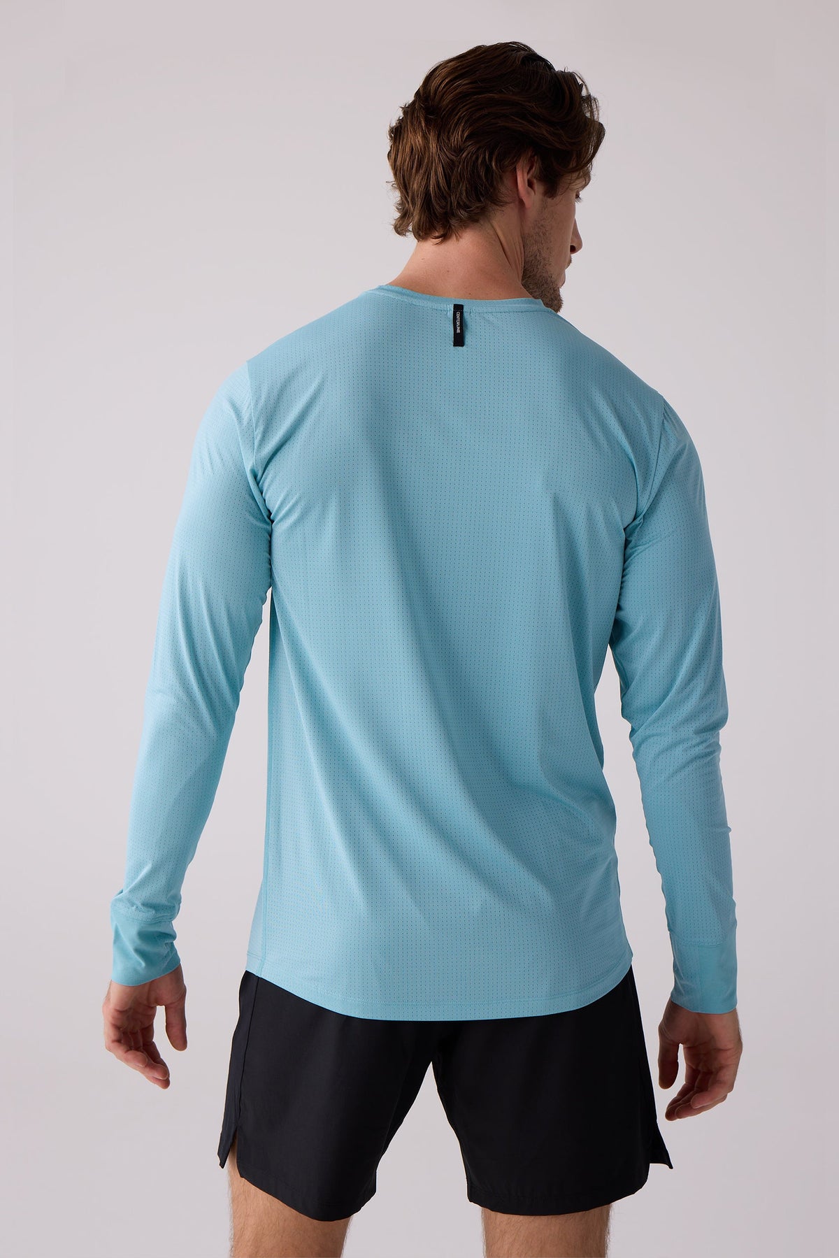 Light blue perforated men's long sleeve shirt by AirLite, back view, with subtle texture and crew neck, worn with black shorts.