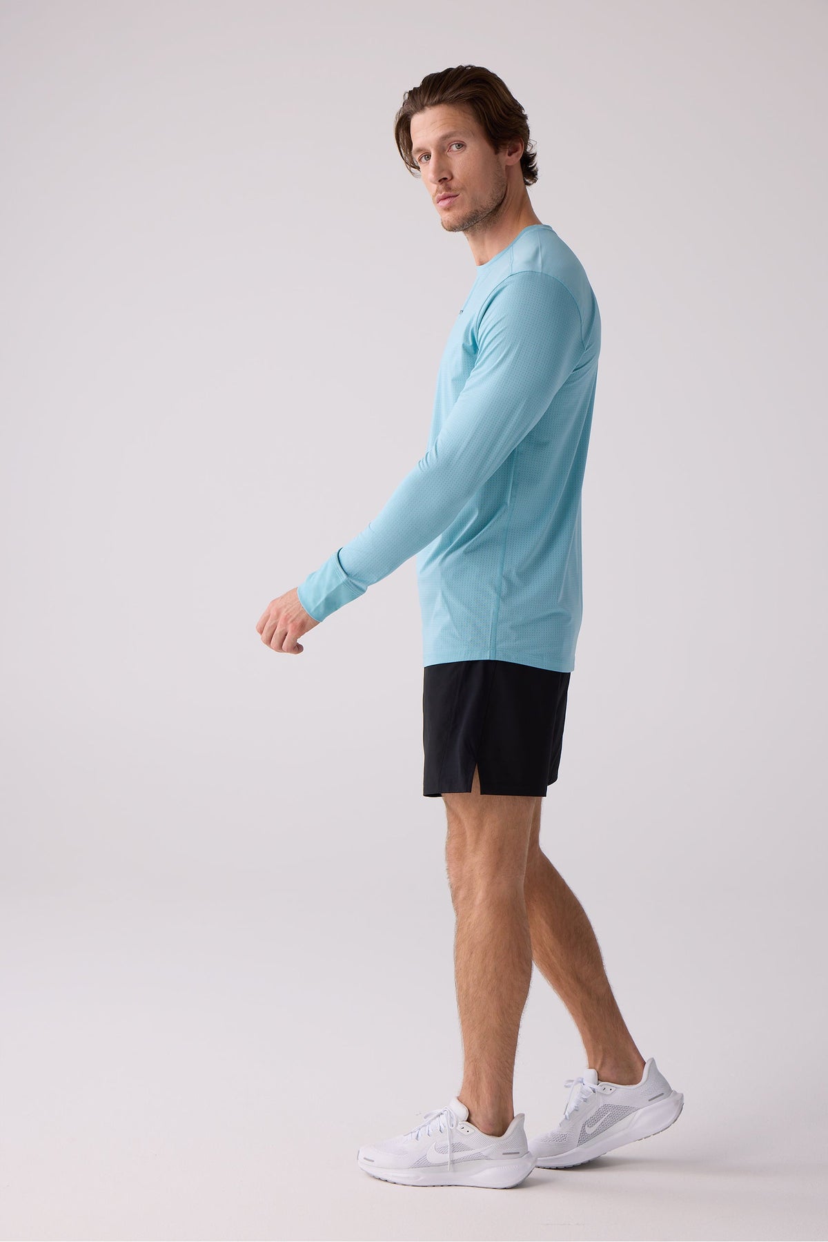 Light blue men's long sleeve performance shirt with textured mesh fabric, side view on model wearing black shorts and white sneakers.