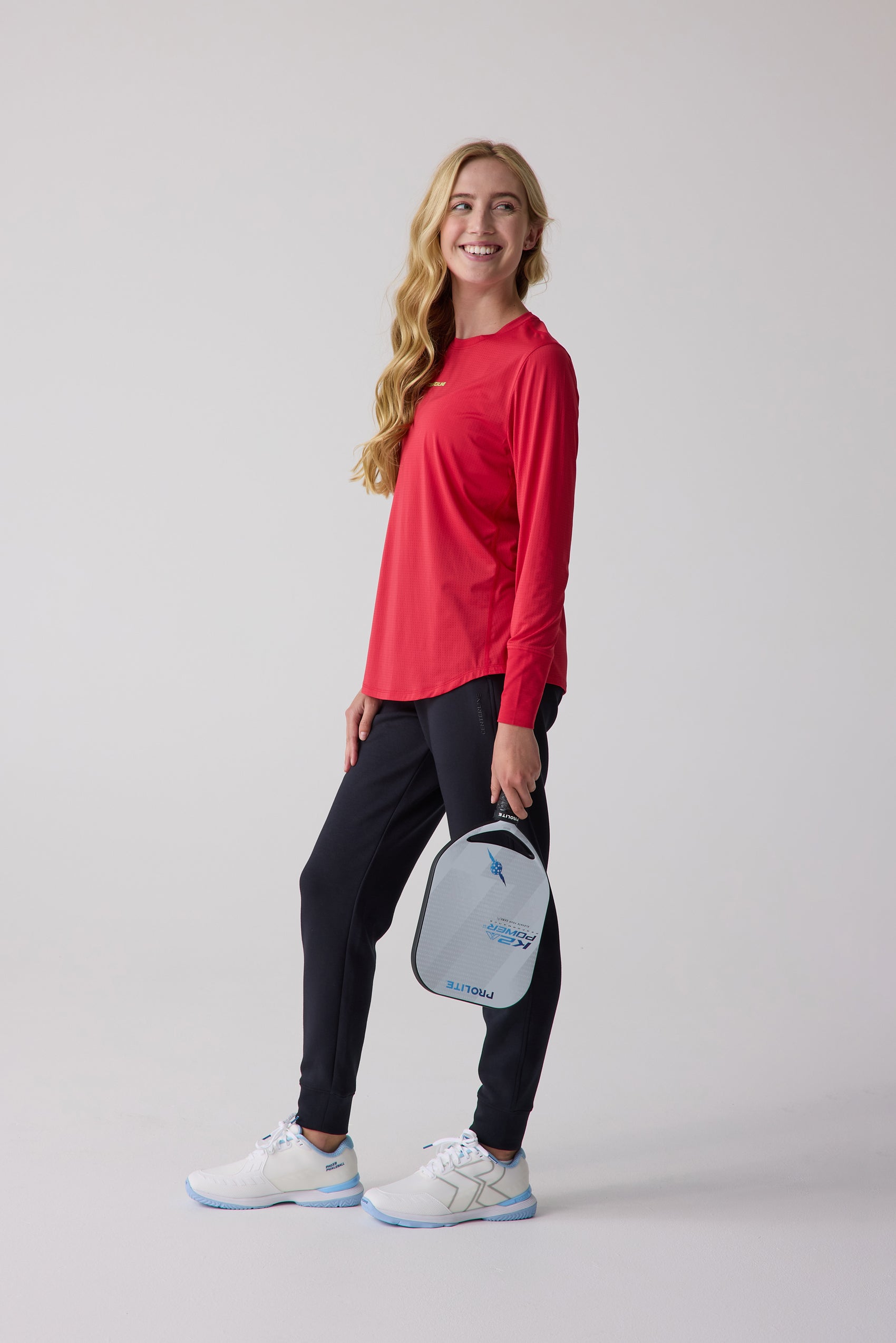 Red women's long-sleeve shirt from Centerline Athletics, featuring subtle textured fabric, worn by a woman holding a pickleball paddle.