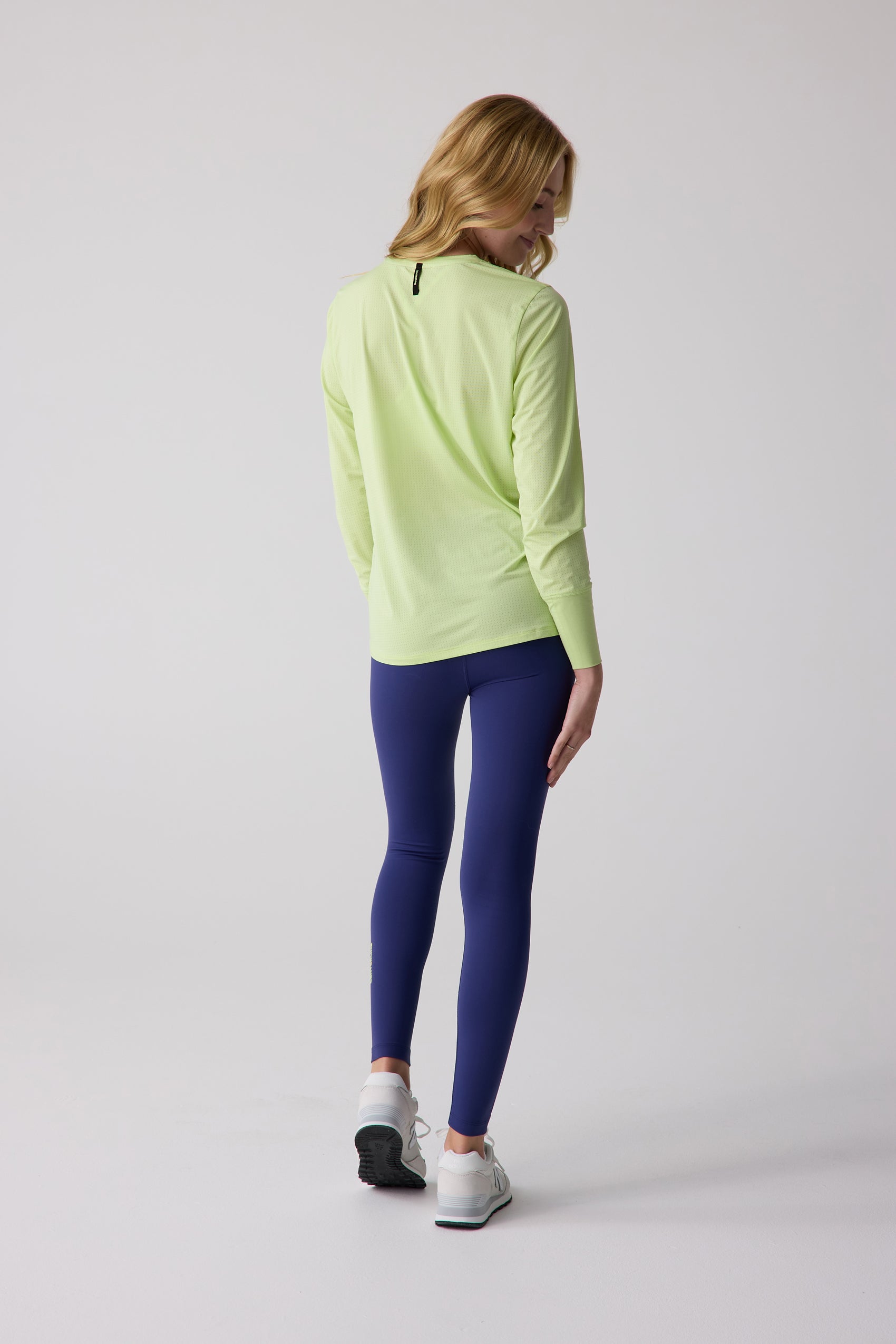 Light green perforated long sleeve shirt by Centerline Athletics, with black neck tag, worn by a woman in navy leggings, back view.