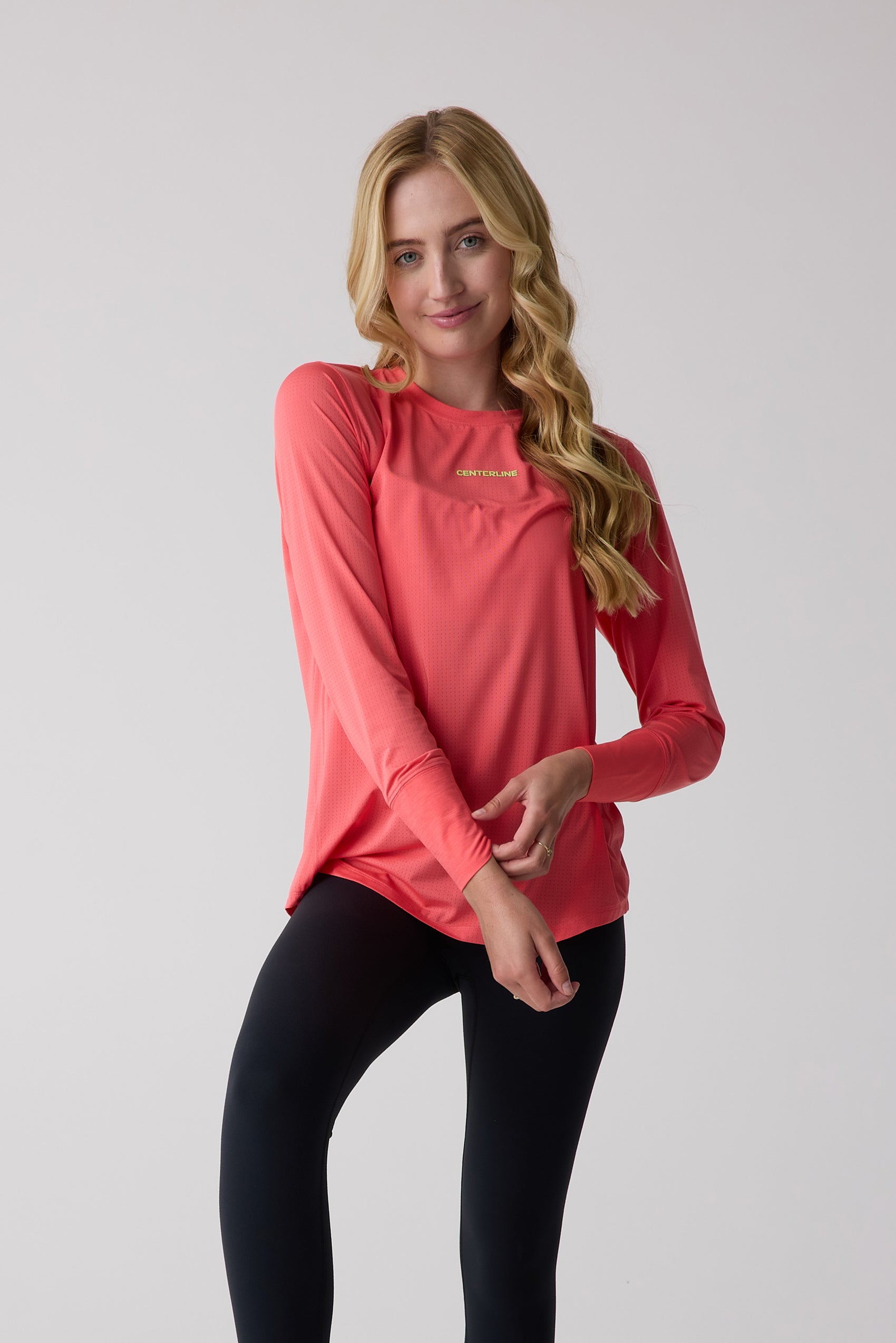 Women's coral perforated long sleeve shirt by Centerline Athletics with a logo on the chest, worn by a model in black leggings.