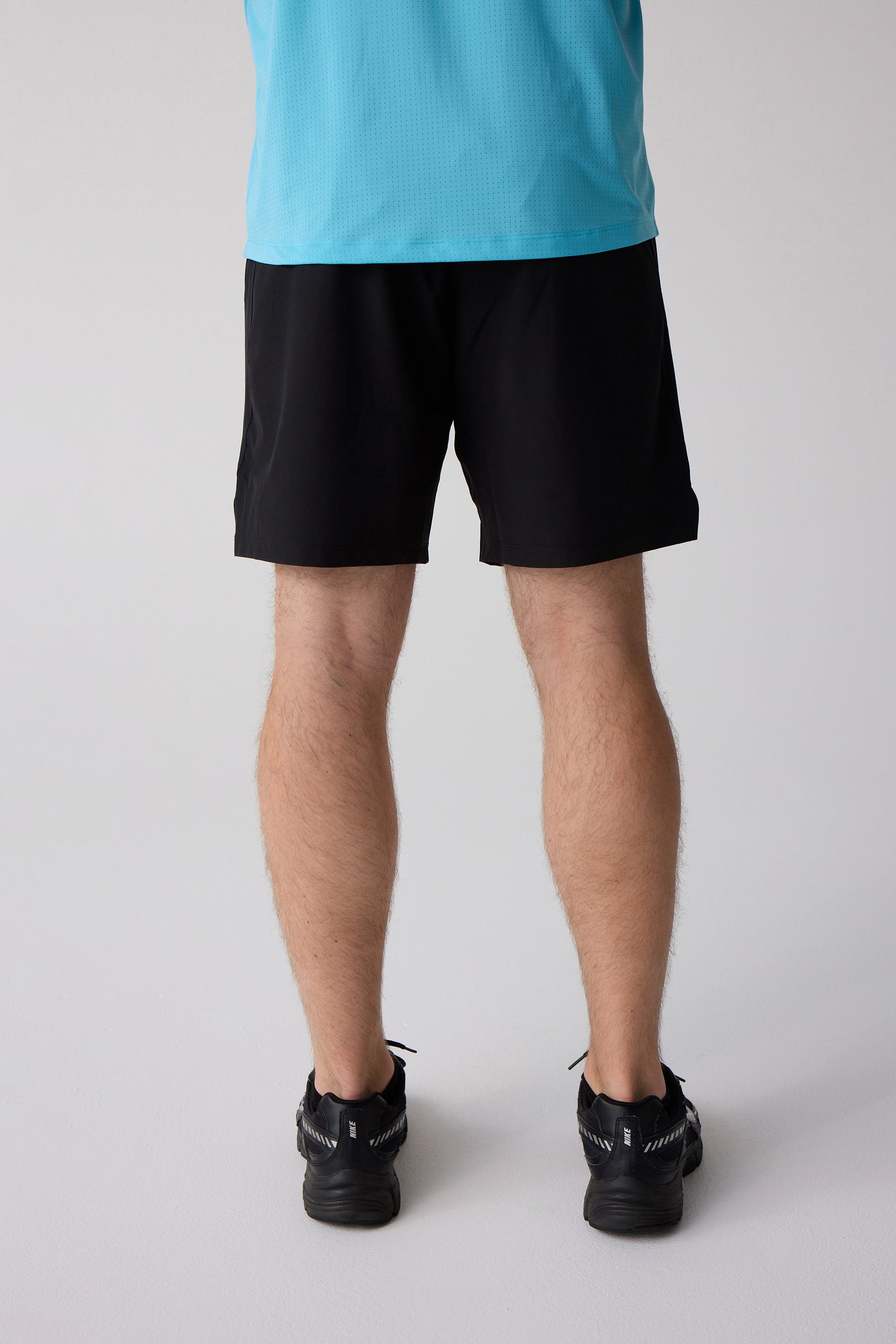 Black 7-inch men's shorts by Centerline Athletics, back view, worn with a light blue perforated shirt and black sneakers.