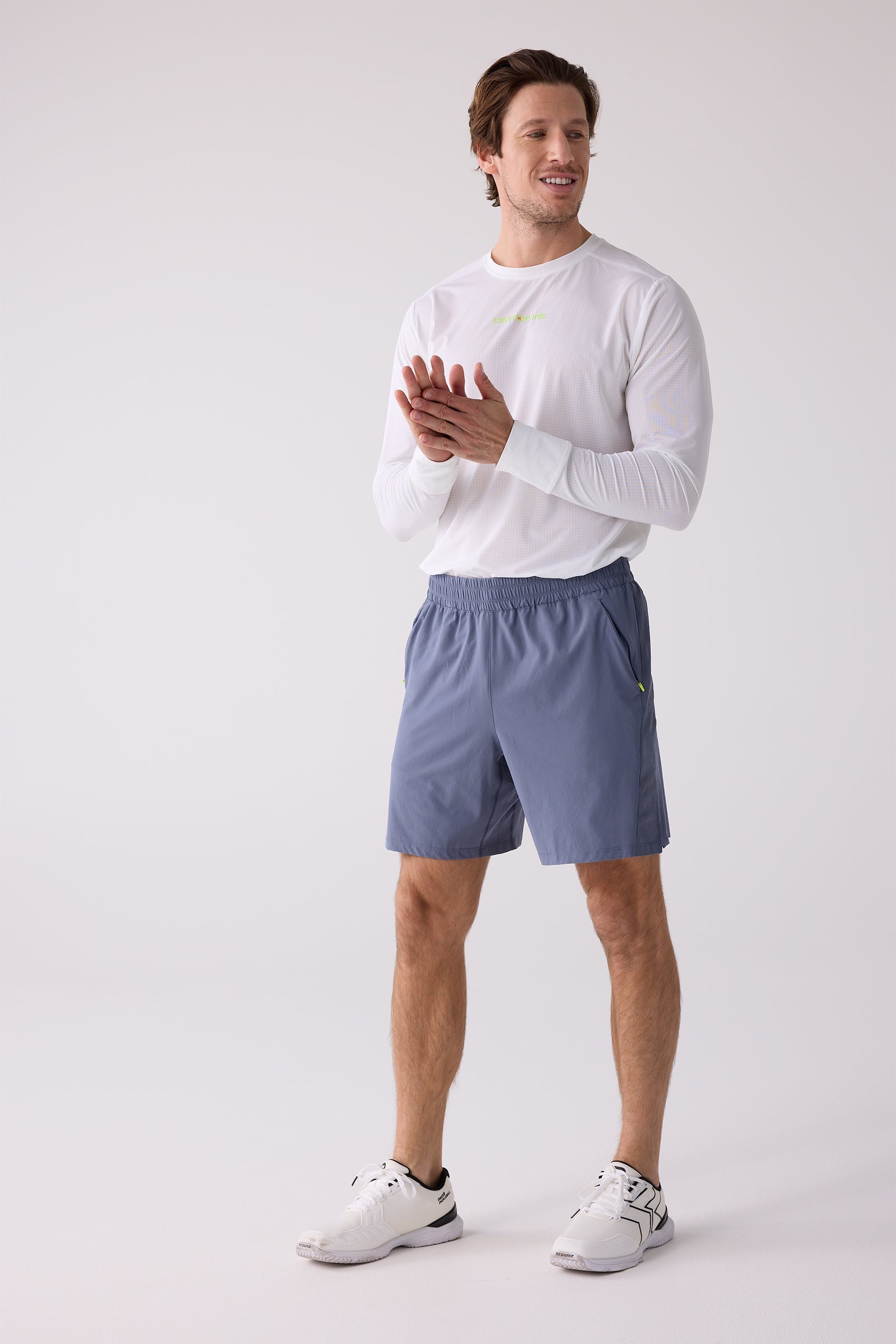 Blue-grey 7-inch men's shorts by Centerline Athletics, with neon yellow pocket accents, worn with a white long-sleeve top and white athletic shoes.