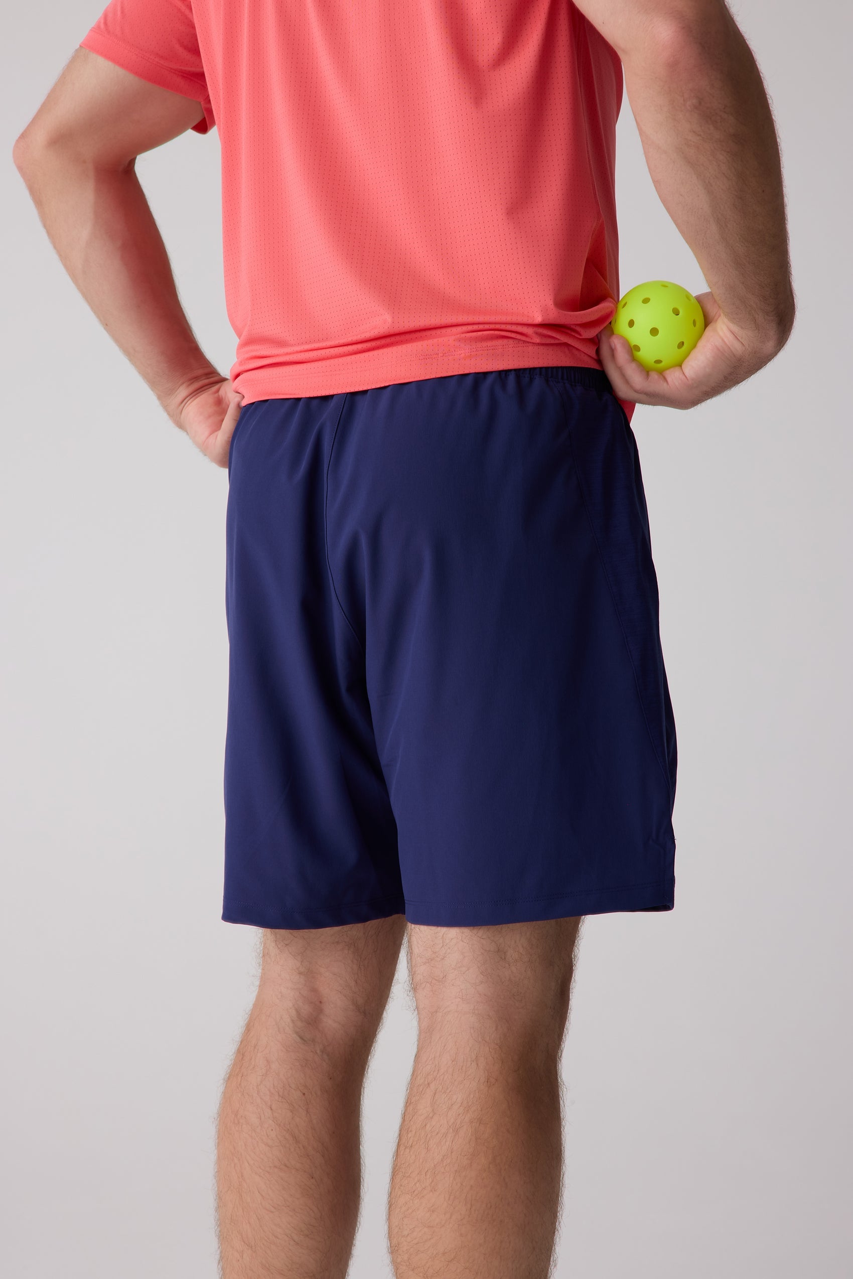 Navy blue AirLite 7" Unlined Short by Centerline Athletics, worn by a man in a coral shirt, holding a pickleball.