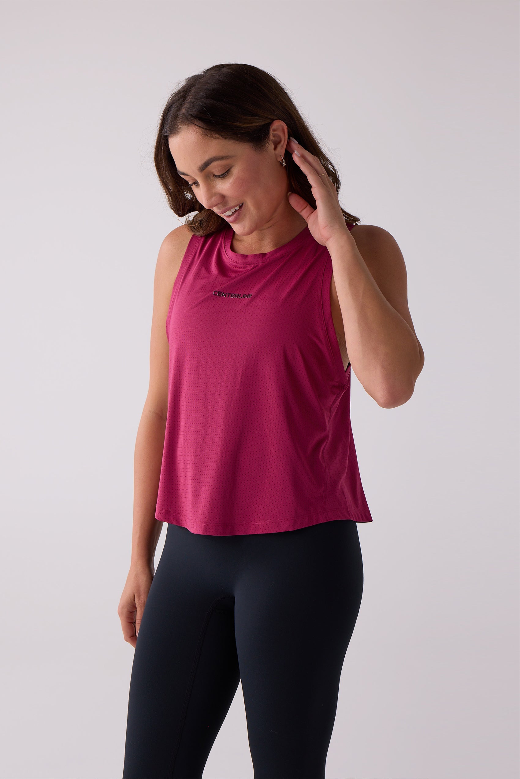Magenta sleeveless perforated tank top by Centerline Athletics with a black chest logo, worn with black leggings.