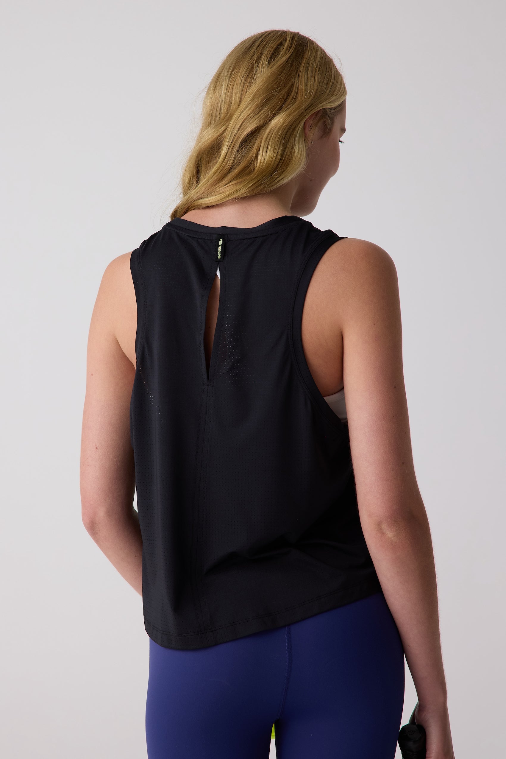 Black AirLite tank by Centerline Athletics with perforated fabric, keyhole back, and 'CENTERLINE' label on the collar, worn over blue leggings.