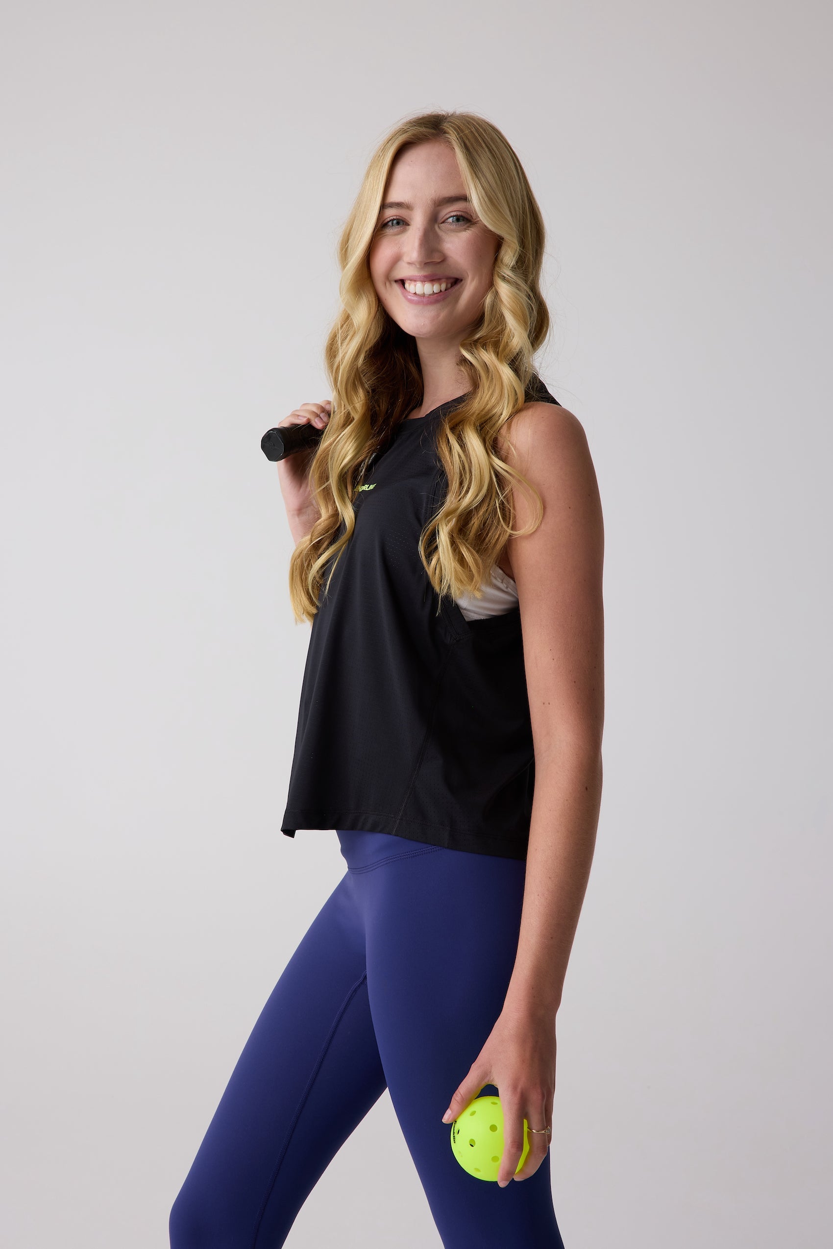 Black cropped AirLite tank by Centerline Athletics, with mesh panels, worn by a woman holding a pickleball and paddle.