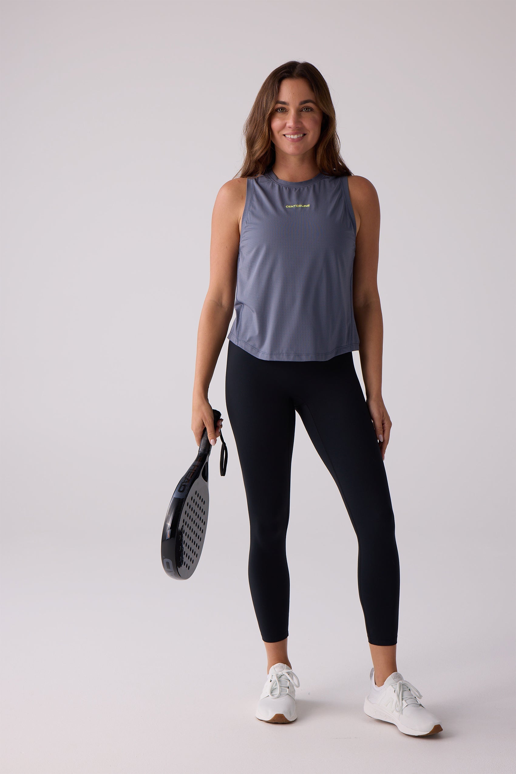 Gray perforated women's AirLite tank top by Centerline Athletics, with yellow CENTERLINE text, worn by a woman holding a black padel racket.
