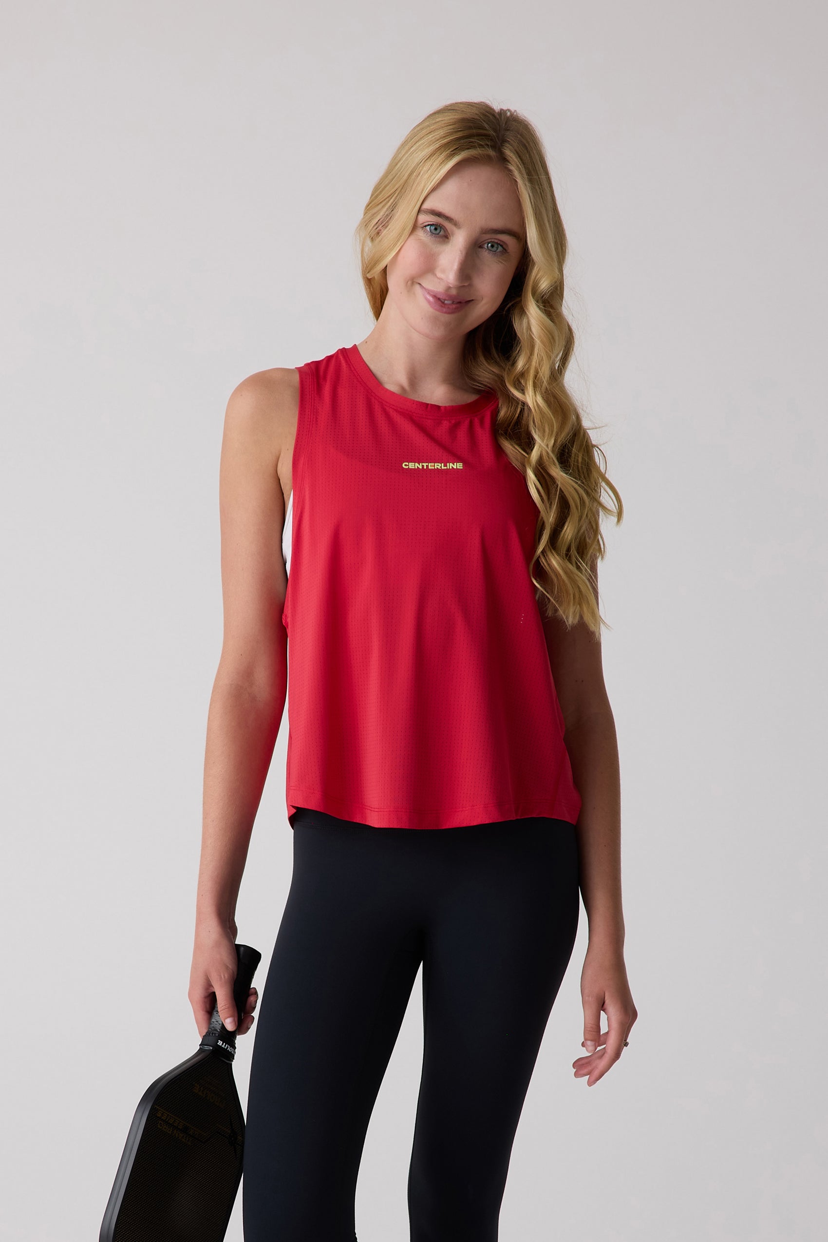 Red AirLite tank top by Centerline Athletics, featuring a perforated texture and gold logo, worn by a woman holding a pickleball paddle.