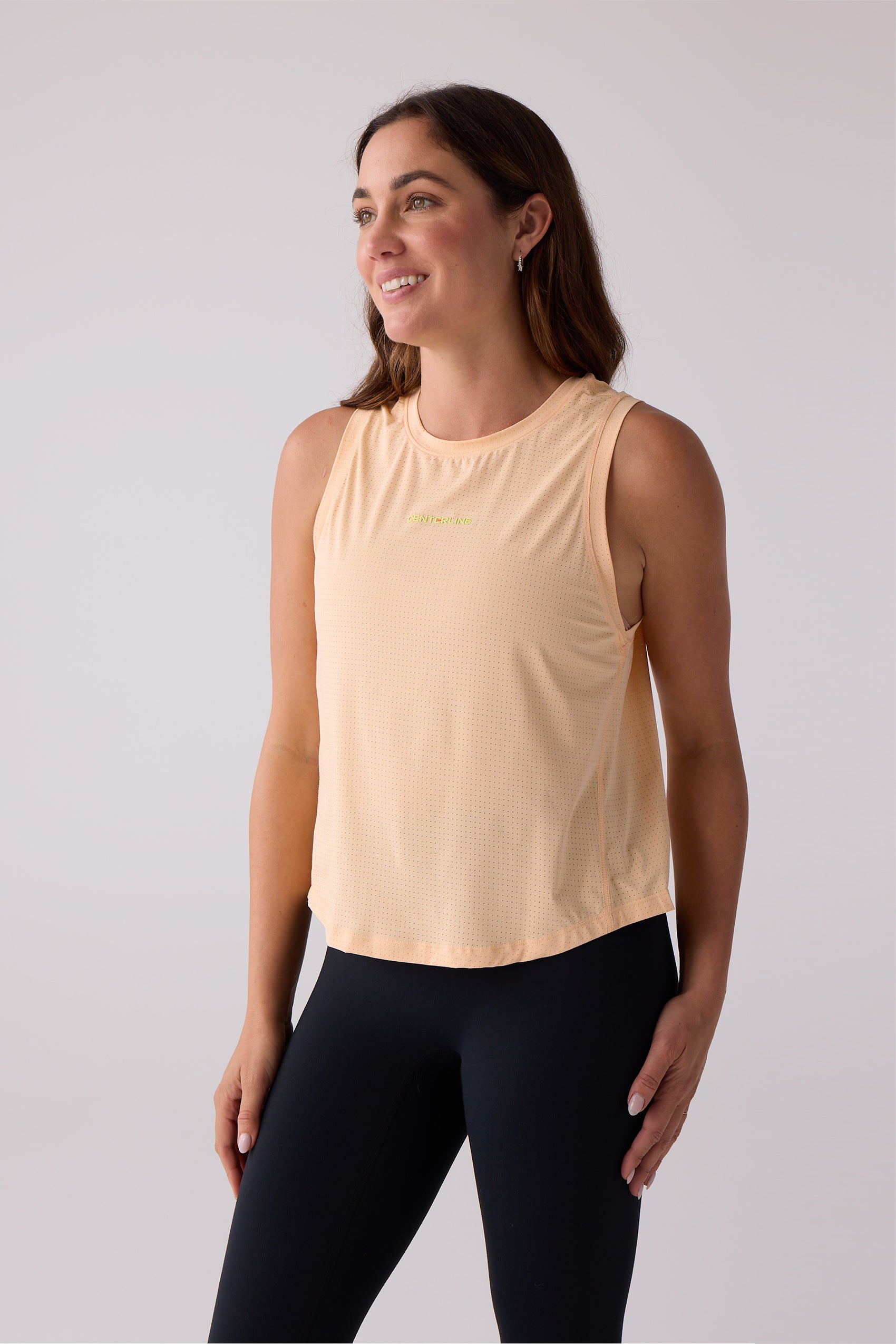 Women's peach AirLite tank top by Centerline Athletics, with perforated texture and yellow logo, paired with black leggings.