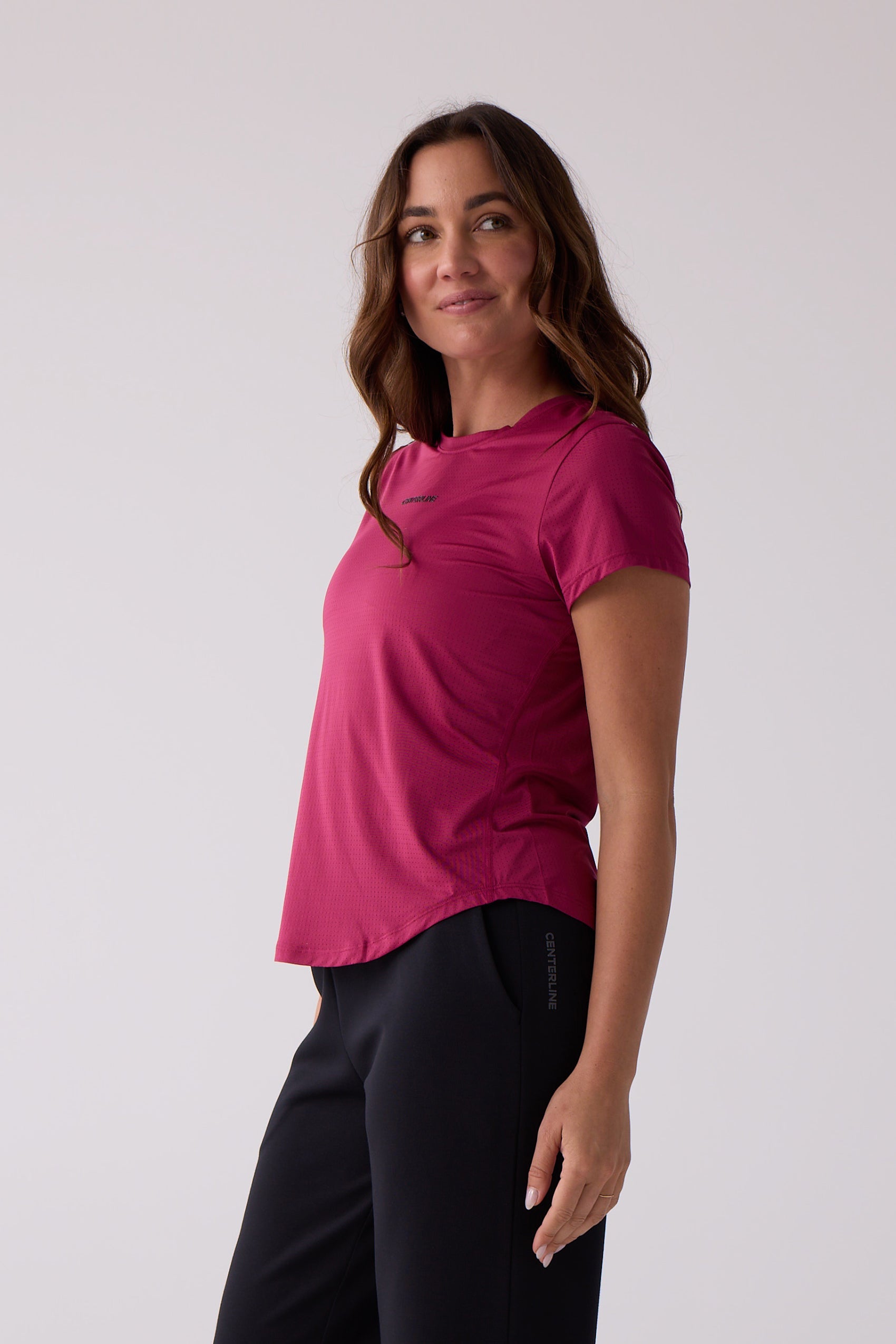 Magenta perforated short sleeve tee by Centerline Athletics, featuring a dark chest logo, on a woman wearing black athletic pants.