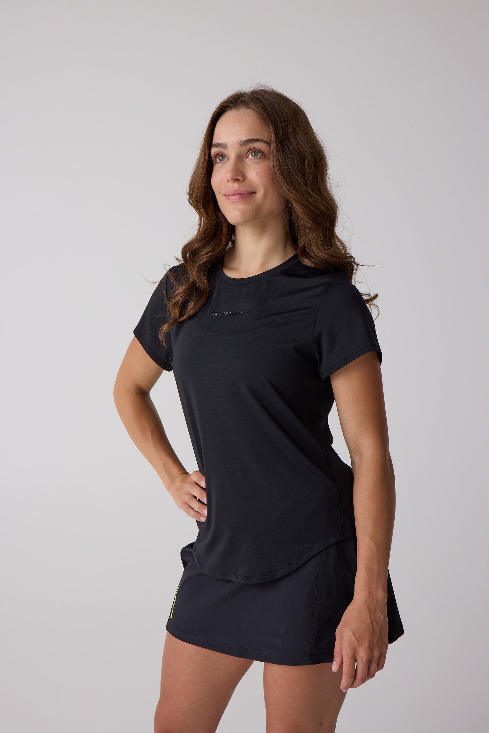 Black short sleeve women's AirLite tee in perforated fabric by Centerline Athletics, featuring a subtle embossed logo, worn with a black skort.