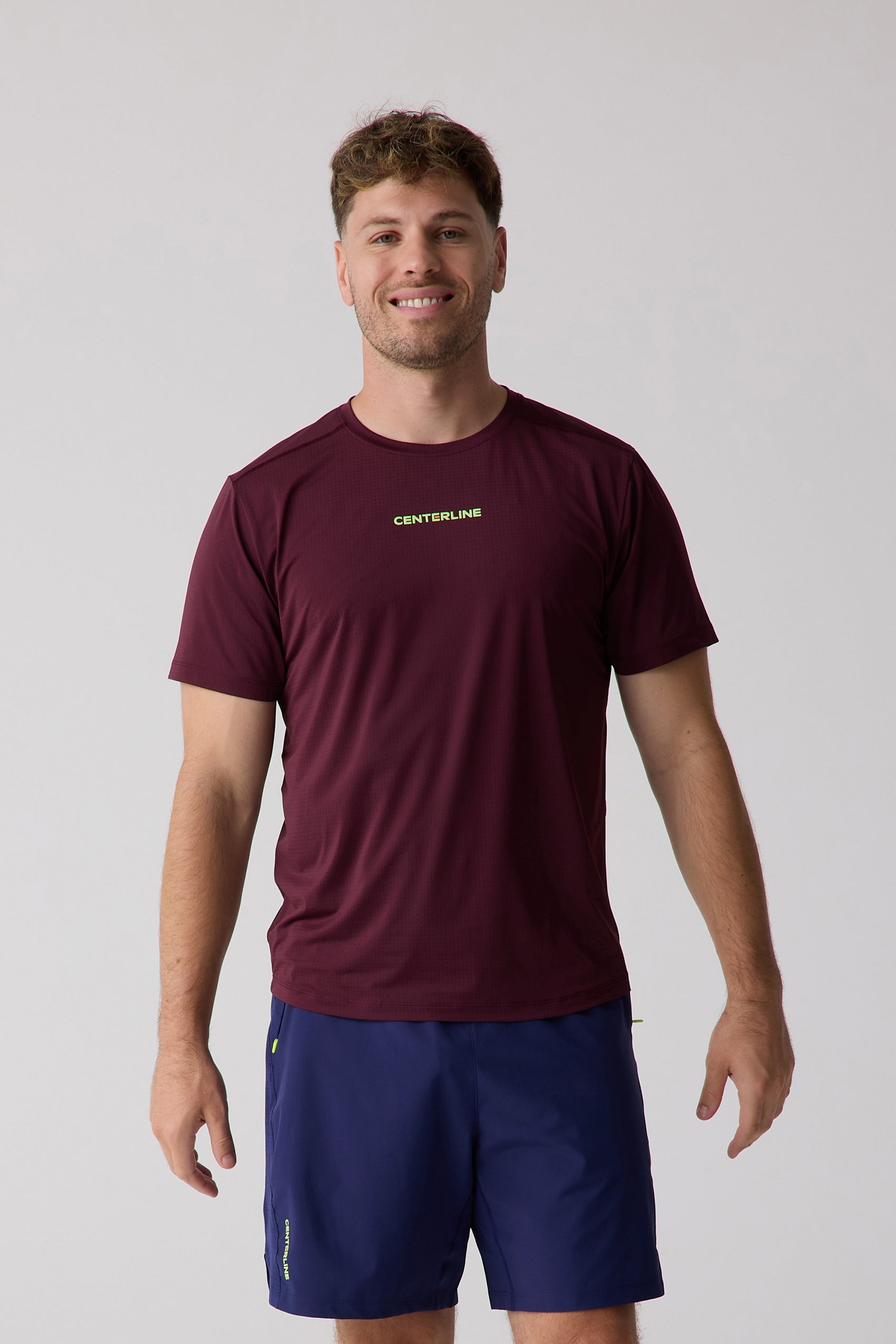 Maroon short sleeve Men's AirLite Tee by Centerline Athletics, featuring a subtle perforated texture and neon green logo, worn by a man.