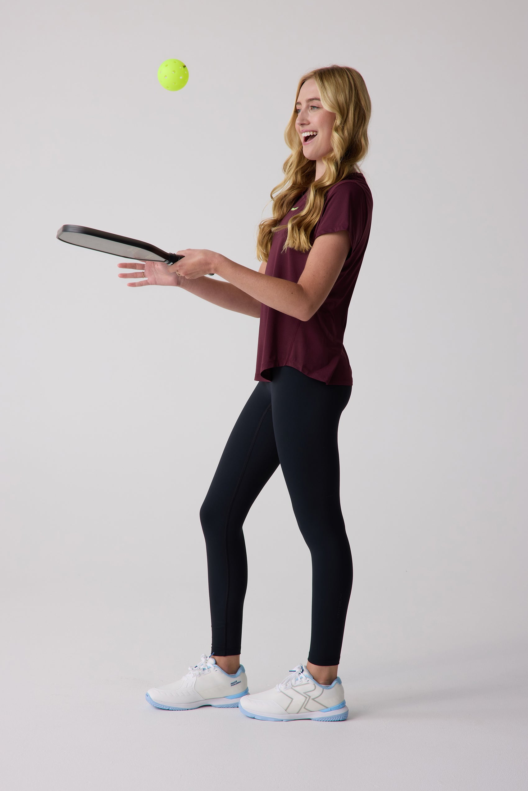 Maroon women's short sleeve tee by Centerline Athletics, worn by a smiling woman holding a pickleball paddle.
