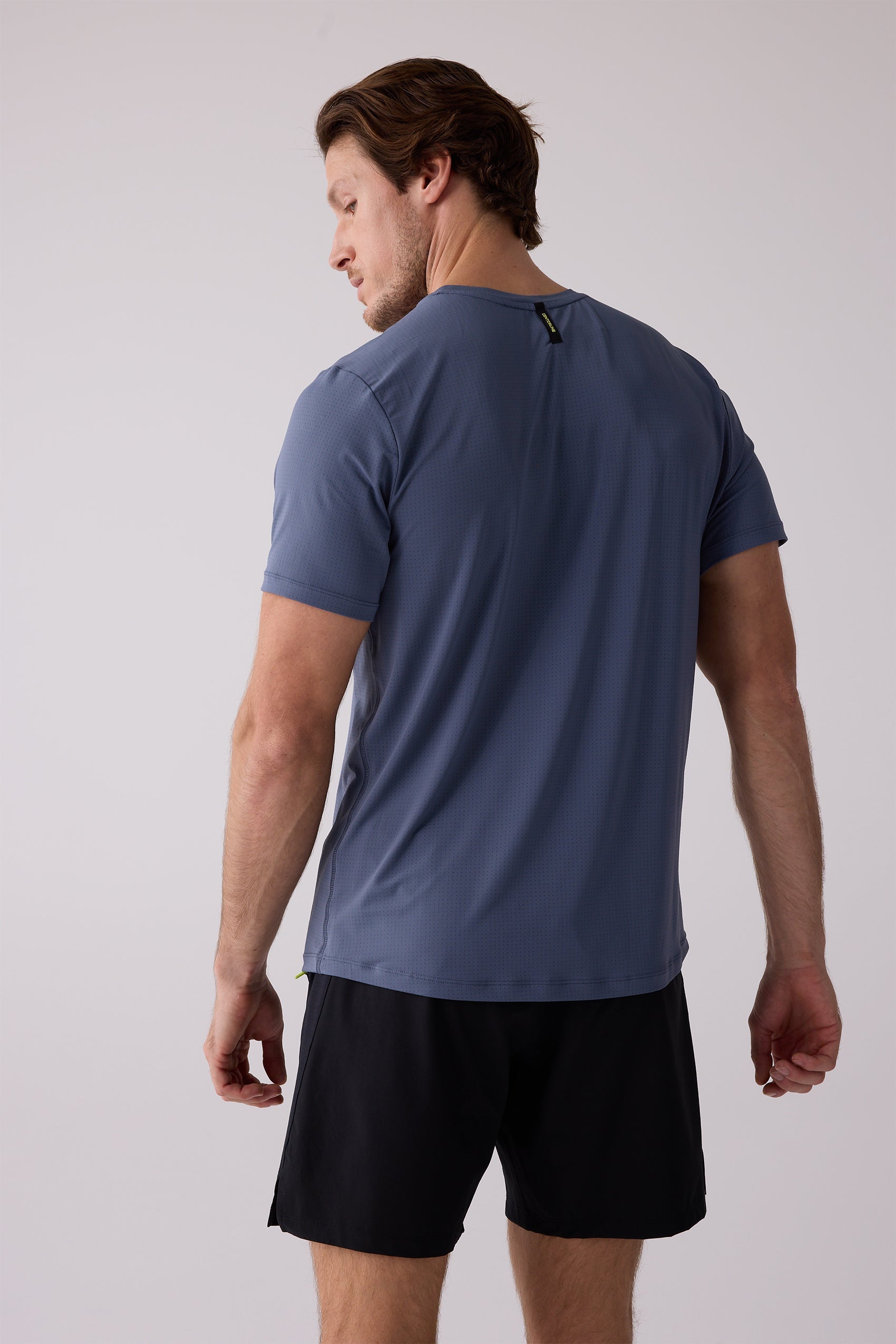 Blue short-sleeve AirLite Tee by Centerline Athletics, featuring a perforated texture and black neck tag, worn from the back with black shorts.