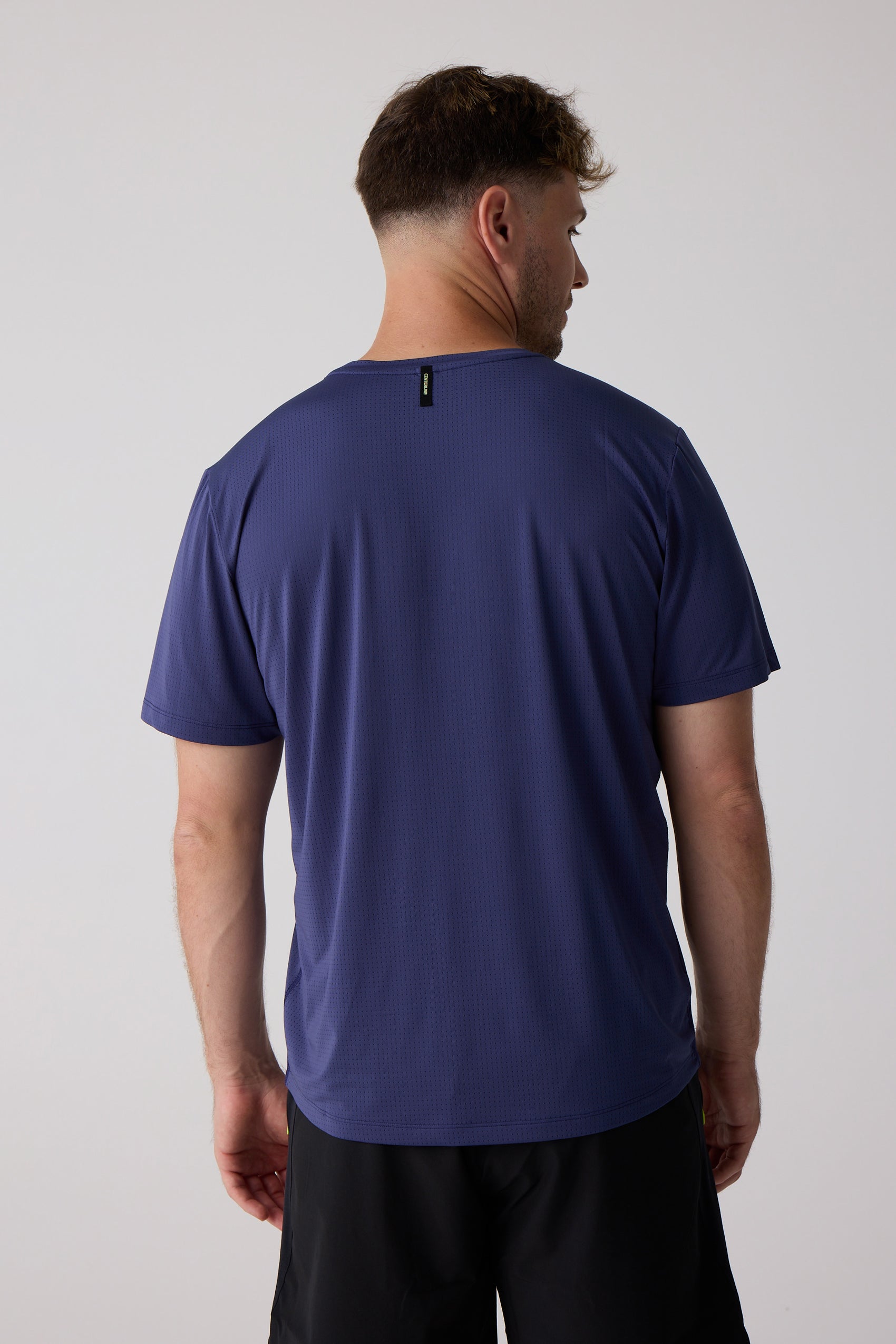 Men's dark purple perforated tee by Centerline Athletics, seen from the back, with a small yellow text tag at the neck.