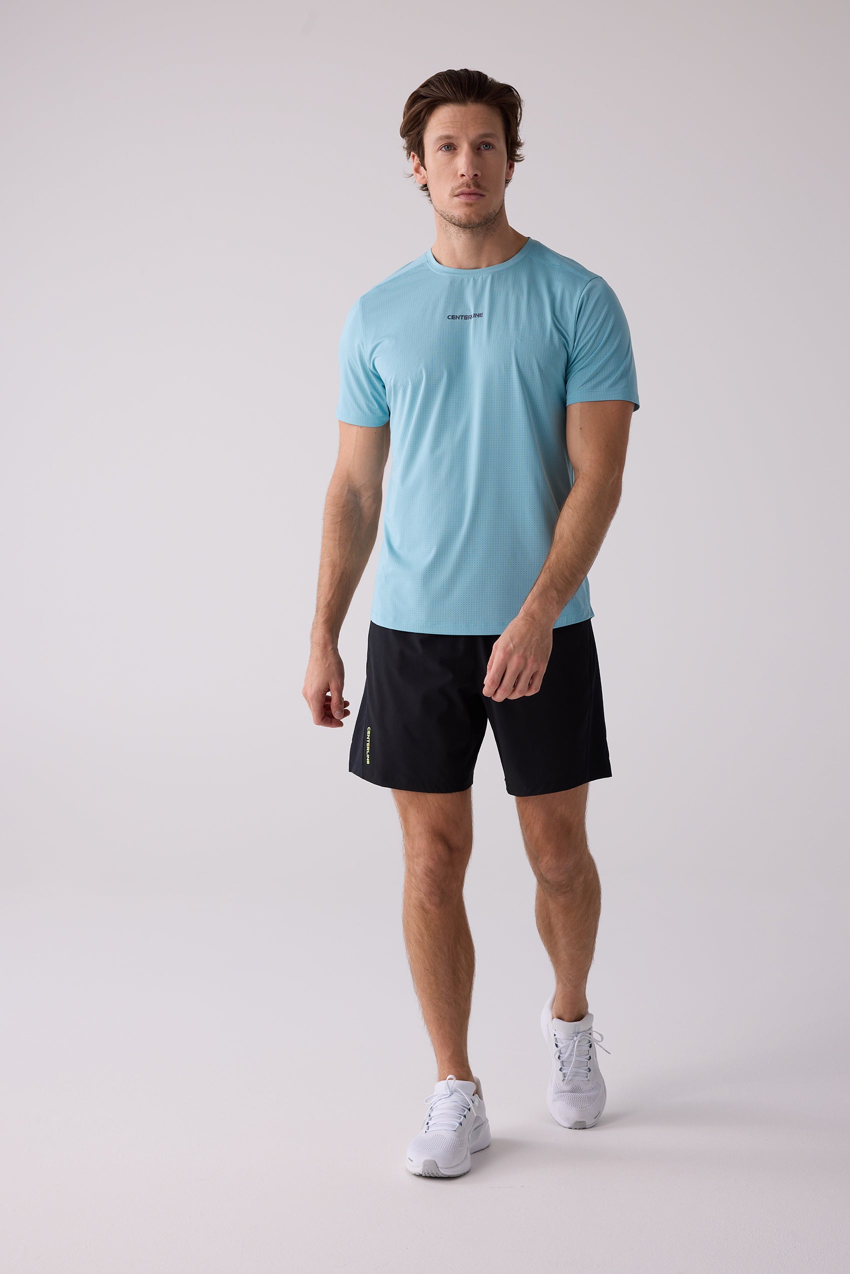 Men's light blue AirLite tee by Centerline Athletics, with perforated texture and black chest logo, modeled with black shorts and white sneakers.