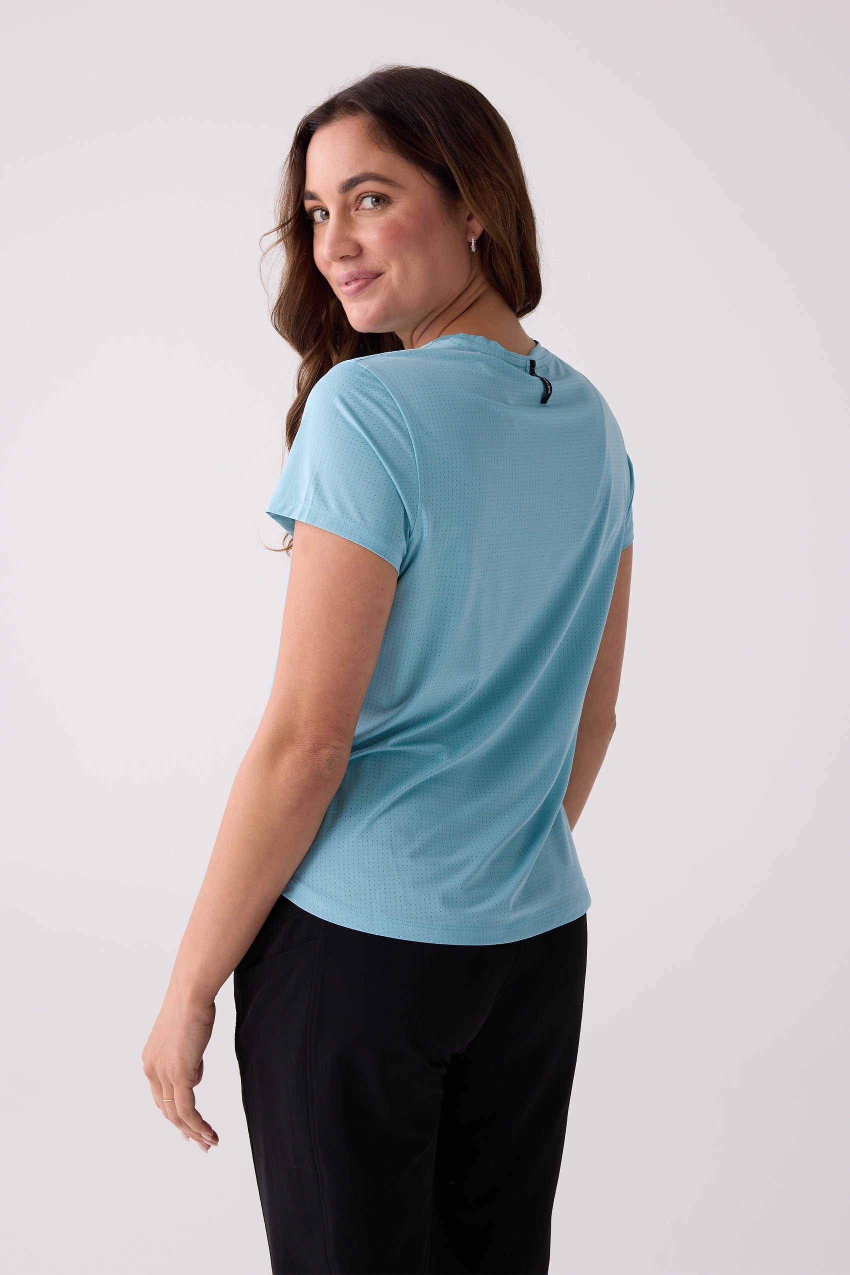 Light blue Women's AirLite Tee by Centerline Athletics, featuring perforated texture and black neck tag, shown from the back on a model.