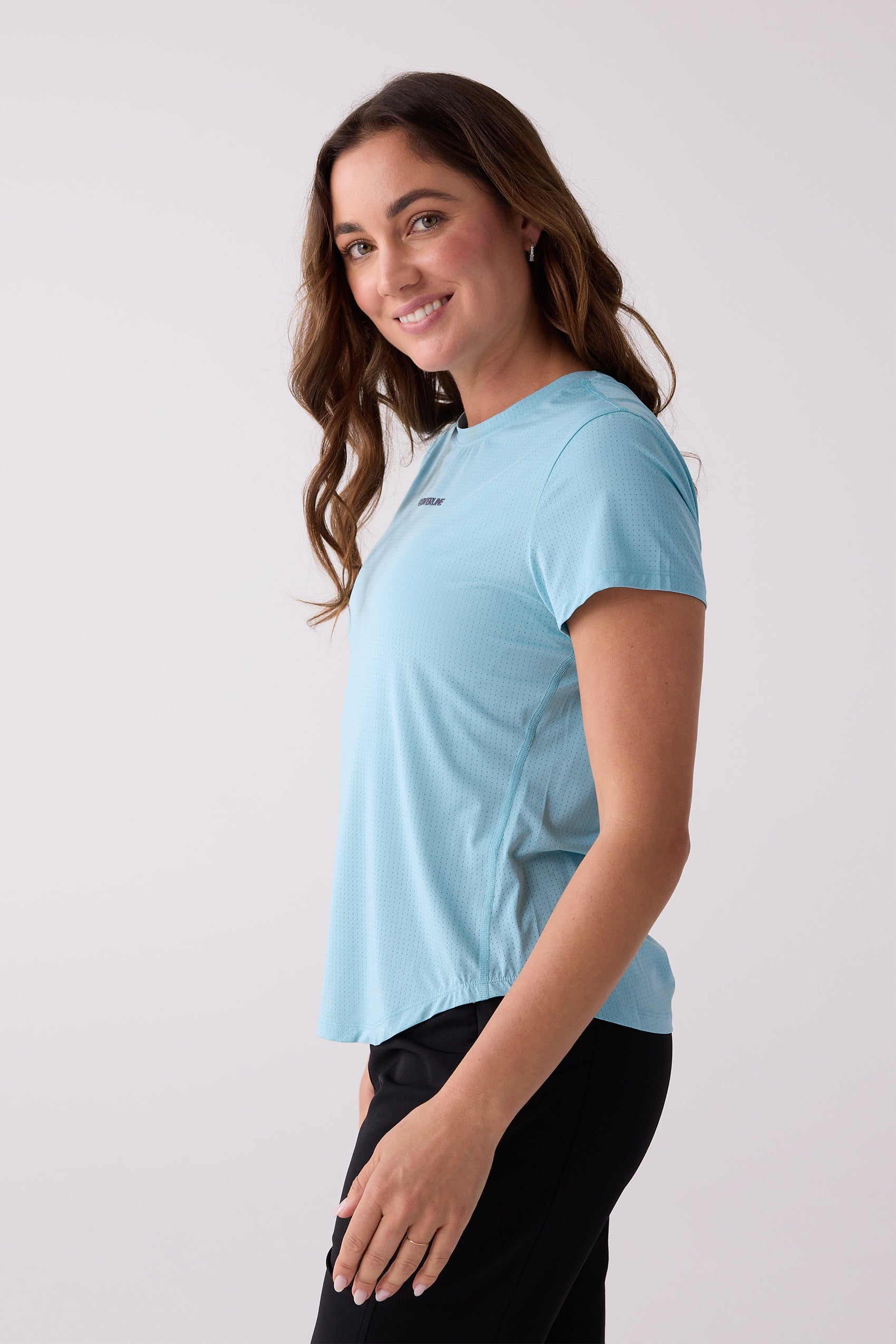 Light blue short sleeve tee by Centerline Athletics, with a perforated texture, small chest logo, side view on a woman in black pants.