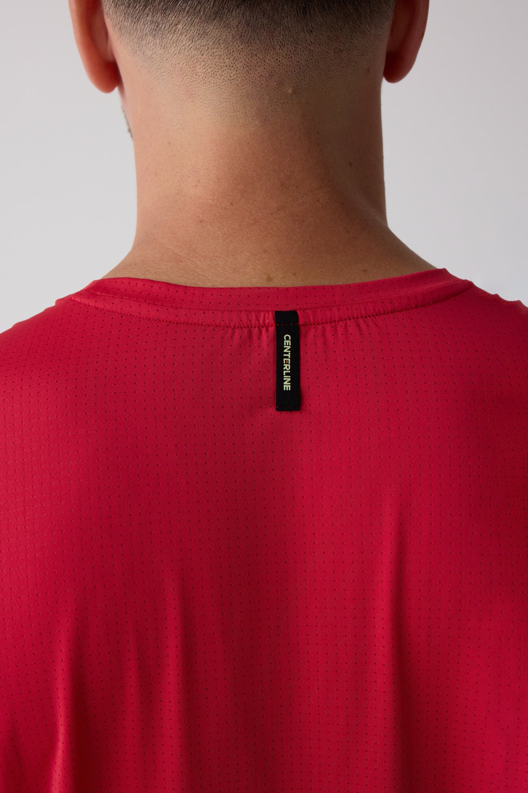 A red Men's AirLite Tee by Centerline Athletics, featuring a perforated texture and a black "CENTERLINE" tag on the back neck.