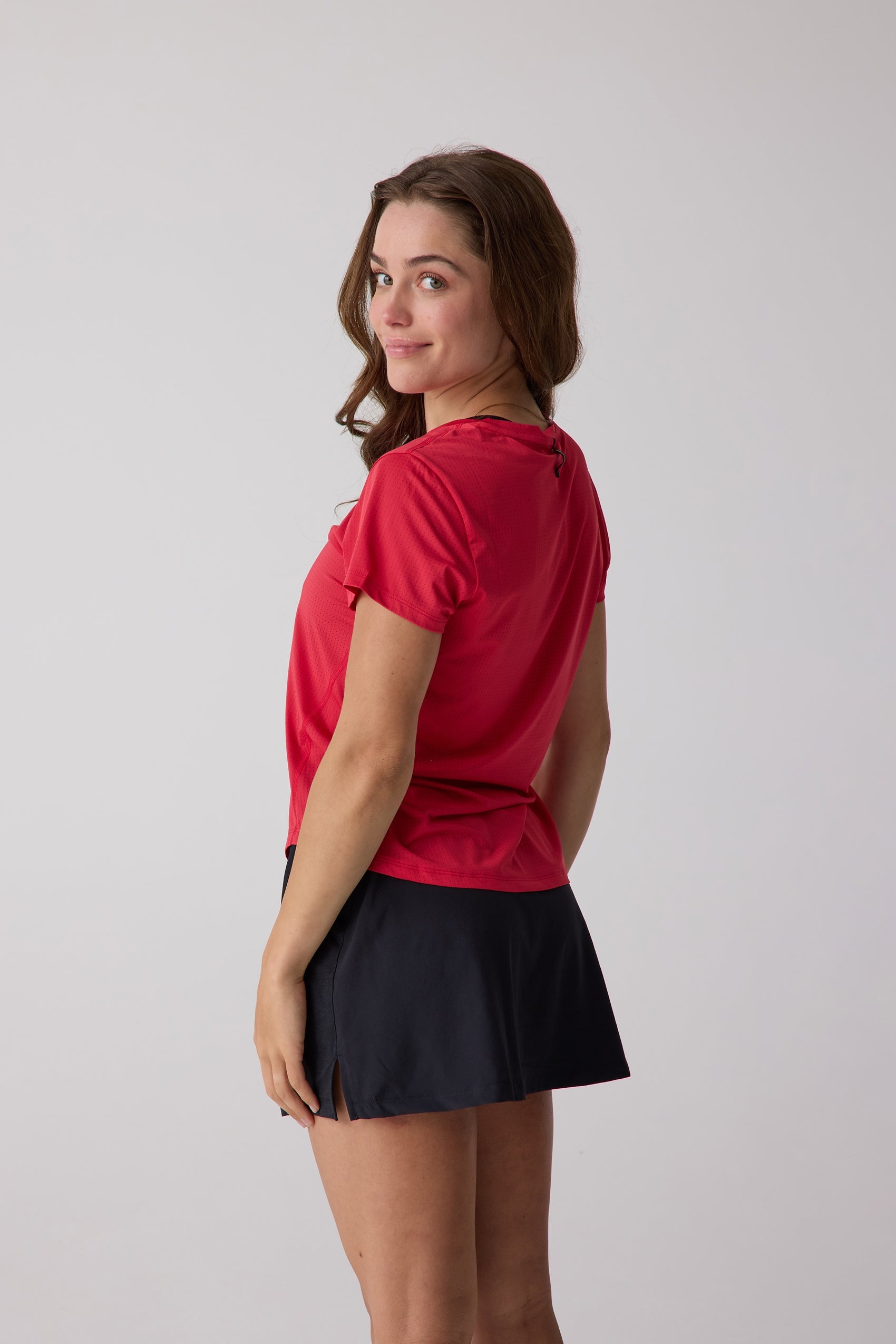 Perforated red short sleeve tee by Centerline Athletics, worn by a model in a partial back view with a black skirt.